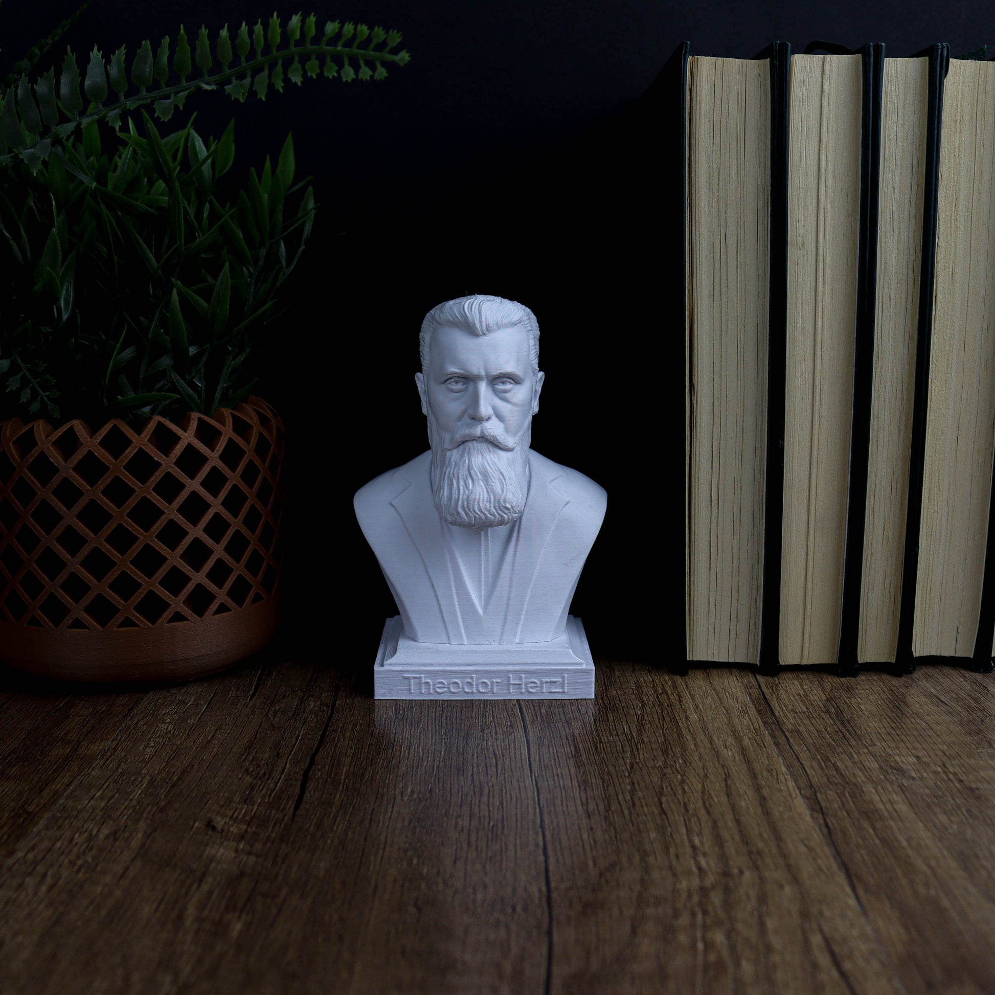 A white bust of a bearded man is displayed on a wooden surface, surrounded by a potted plant and a stack of books.