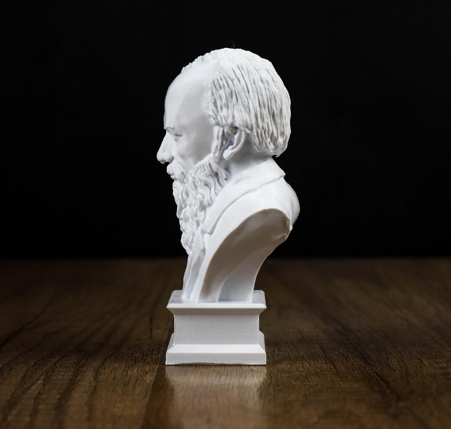 A white bust of a bearded man is displayed on a wooden surface against a black background.