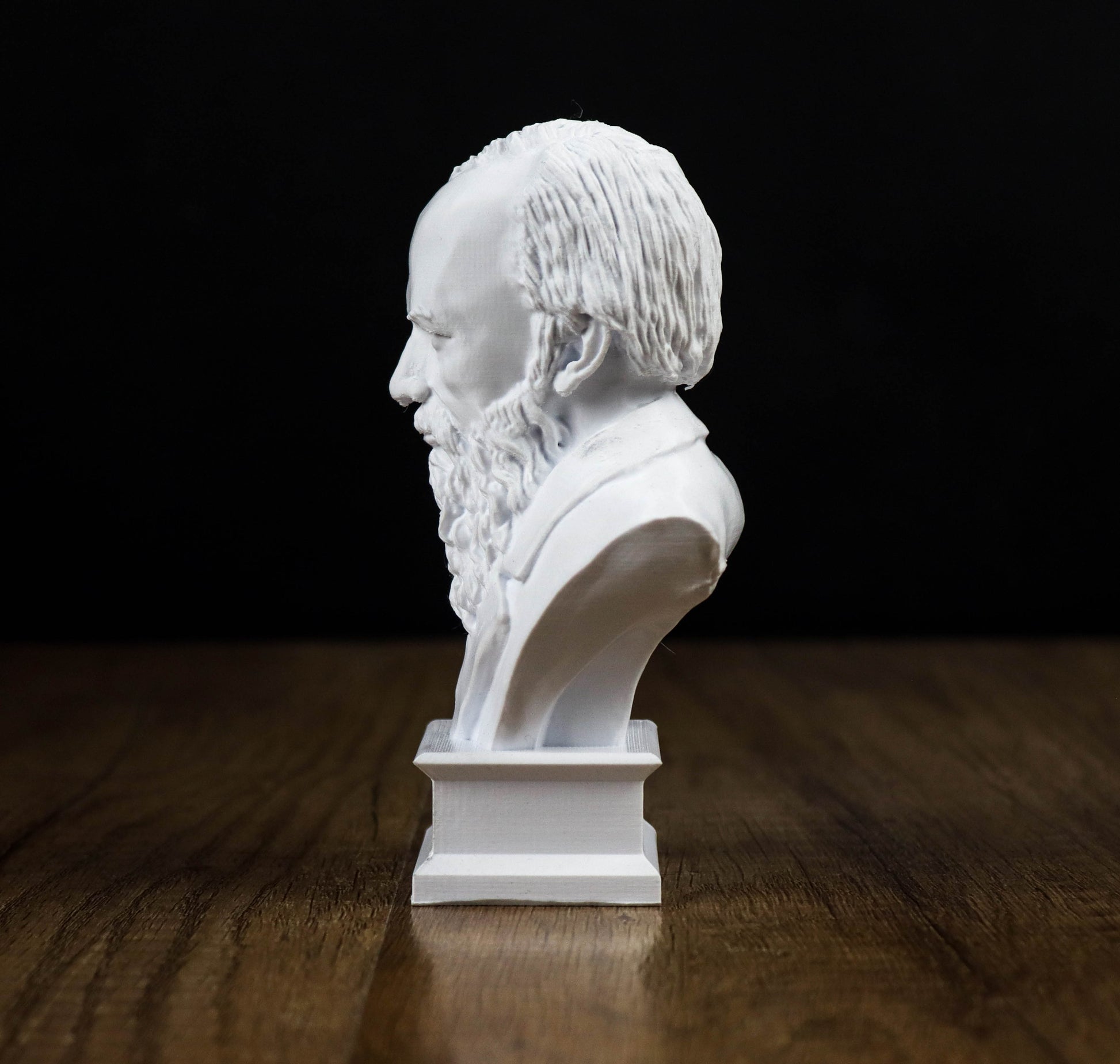 A white bust of a bearded man is displayed on a wooden surface against a black background.