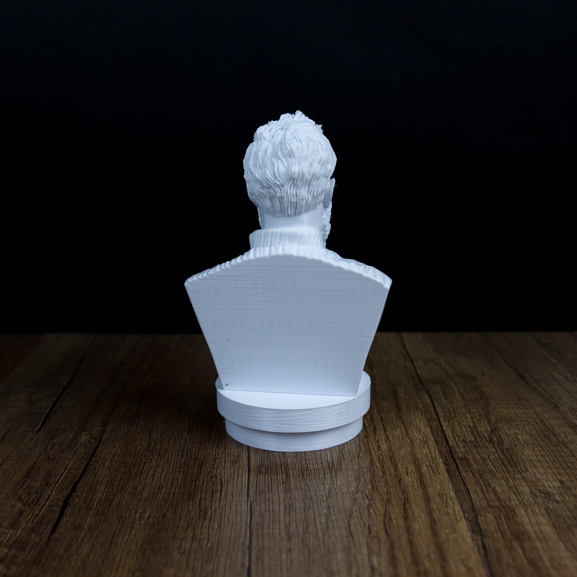 A white bust sculpture is displayed on a wooden surface against a dark background.