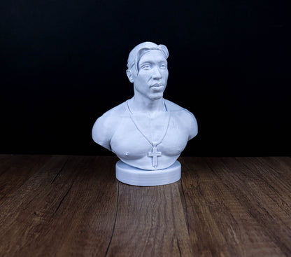 A white bust sculpture of a man with a cross necklace is displayed on a wooden surface against a dark background.