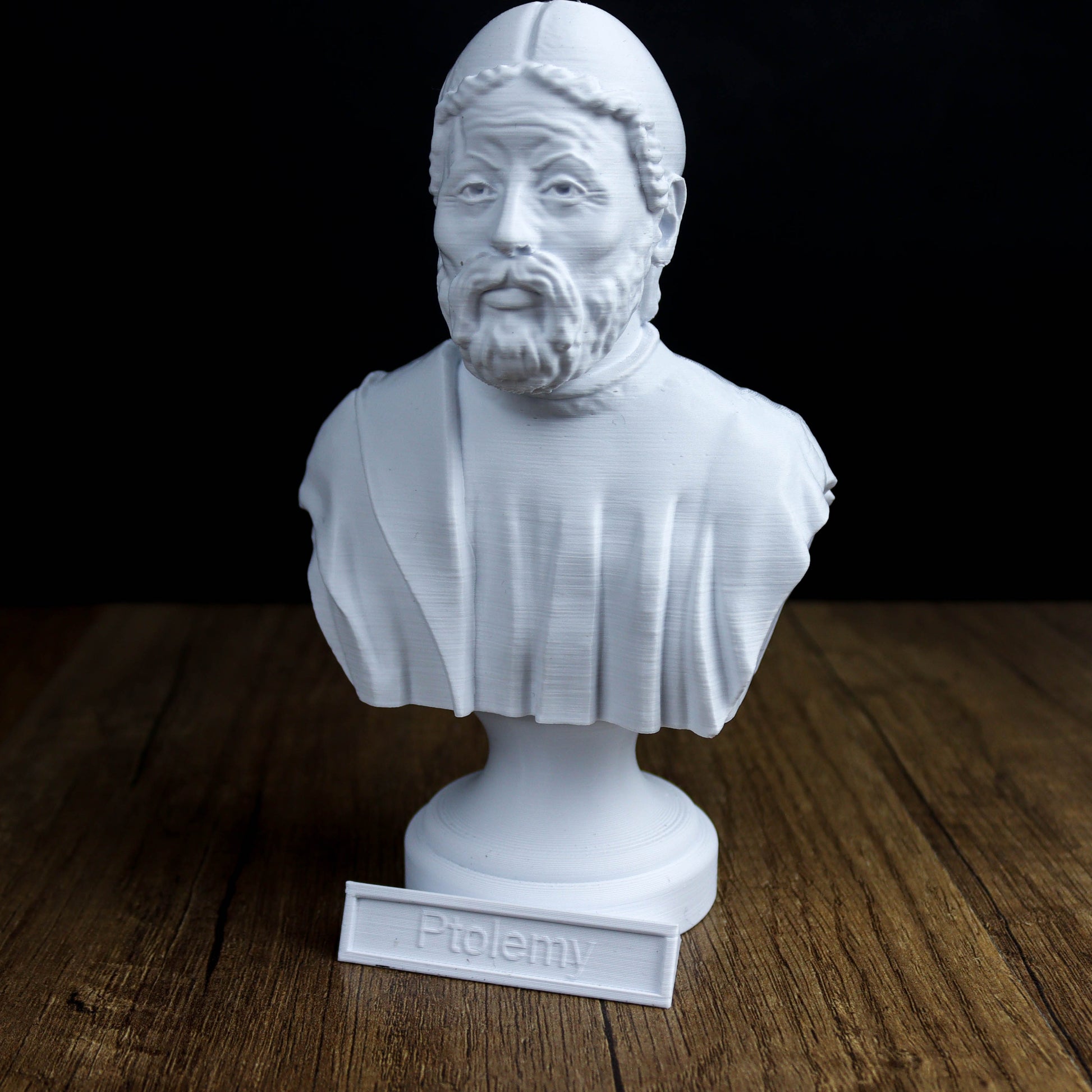 A white bust of a bearded man with a serious expression, placed on a wooden surface.