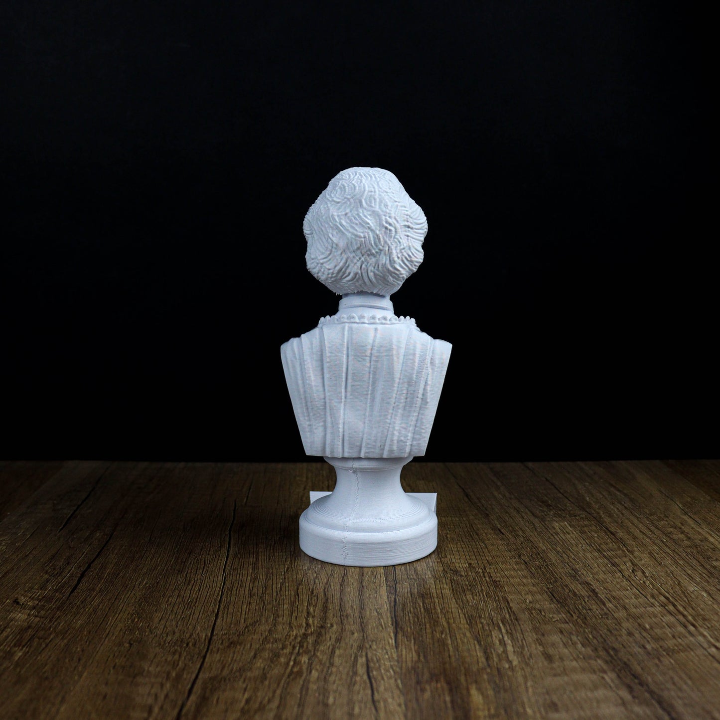 A white bust sculpture is displayed on a wooden surface against a black background.