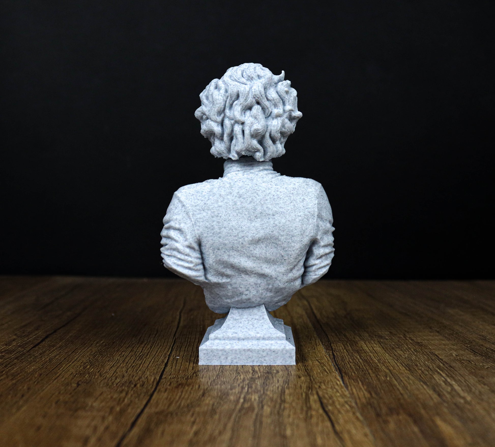 A white stone bust statue of a person sitting on a wooden surface against a black background.