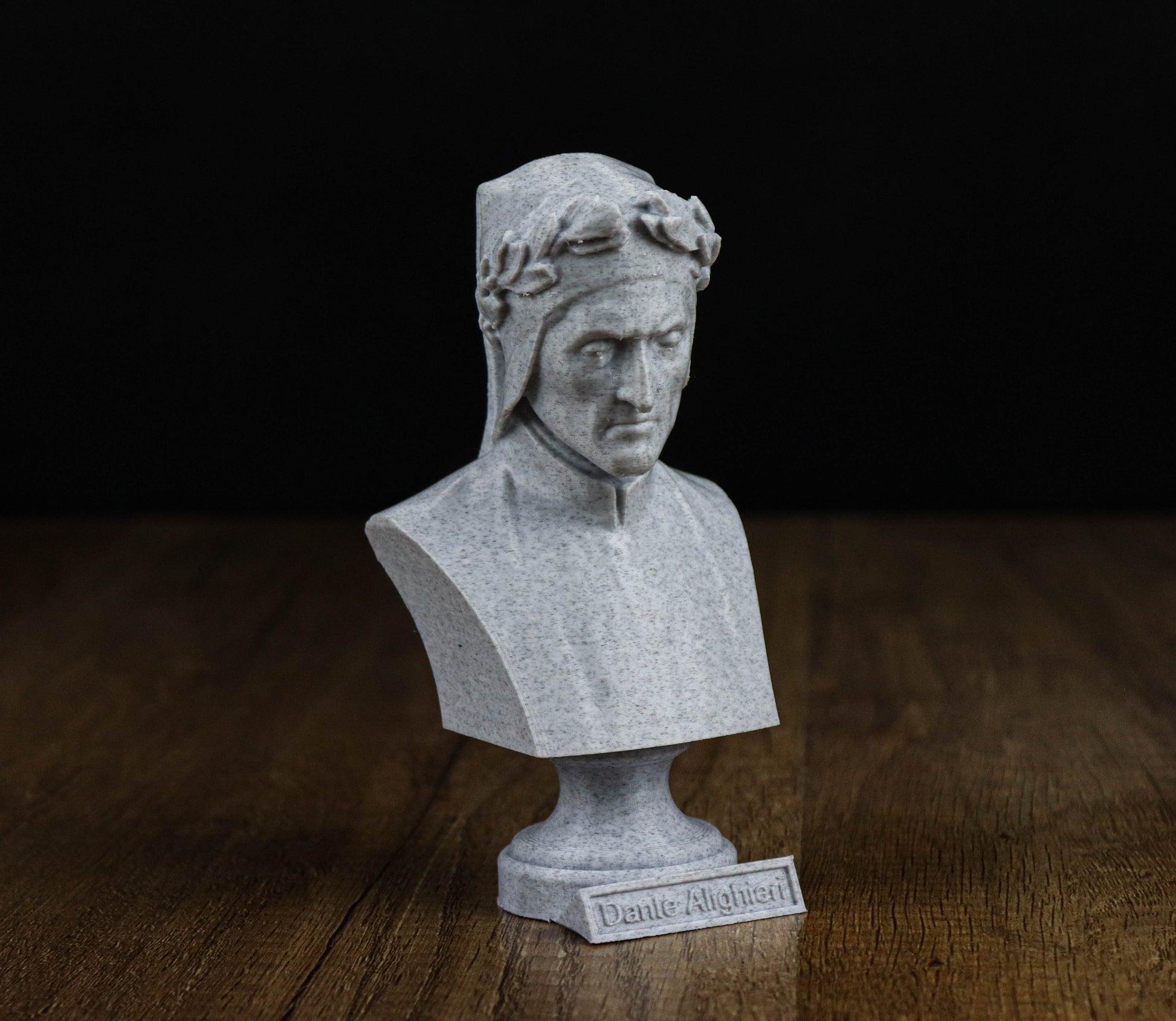 A small bust of a man, possibly a historical figure, is displayed on a wooden surface against a black background.