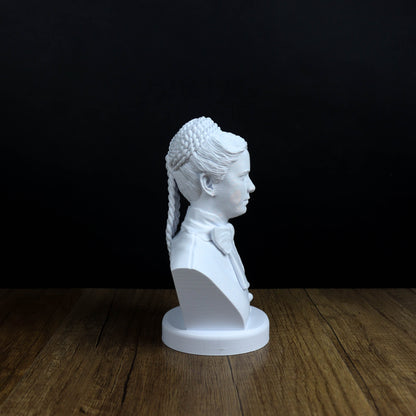 A white bust of a person with braided hair is displayed on a wooden surface against a black background.