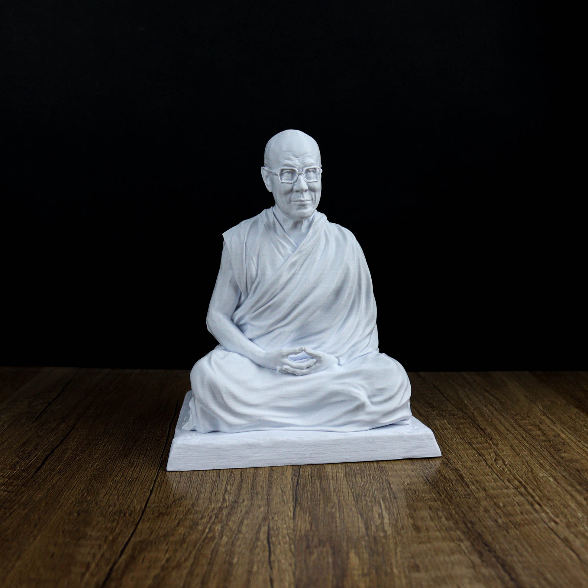 A white statue of a seated Buddha figure on a wooden surface against a black background.