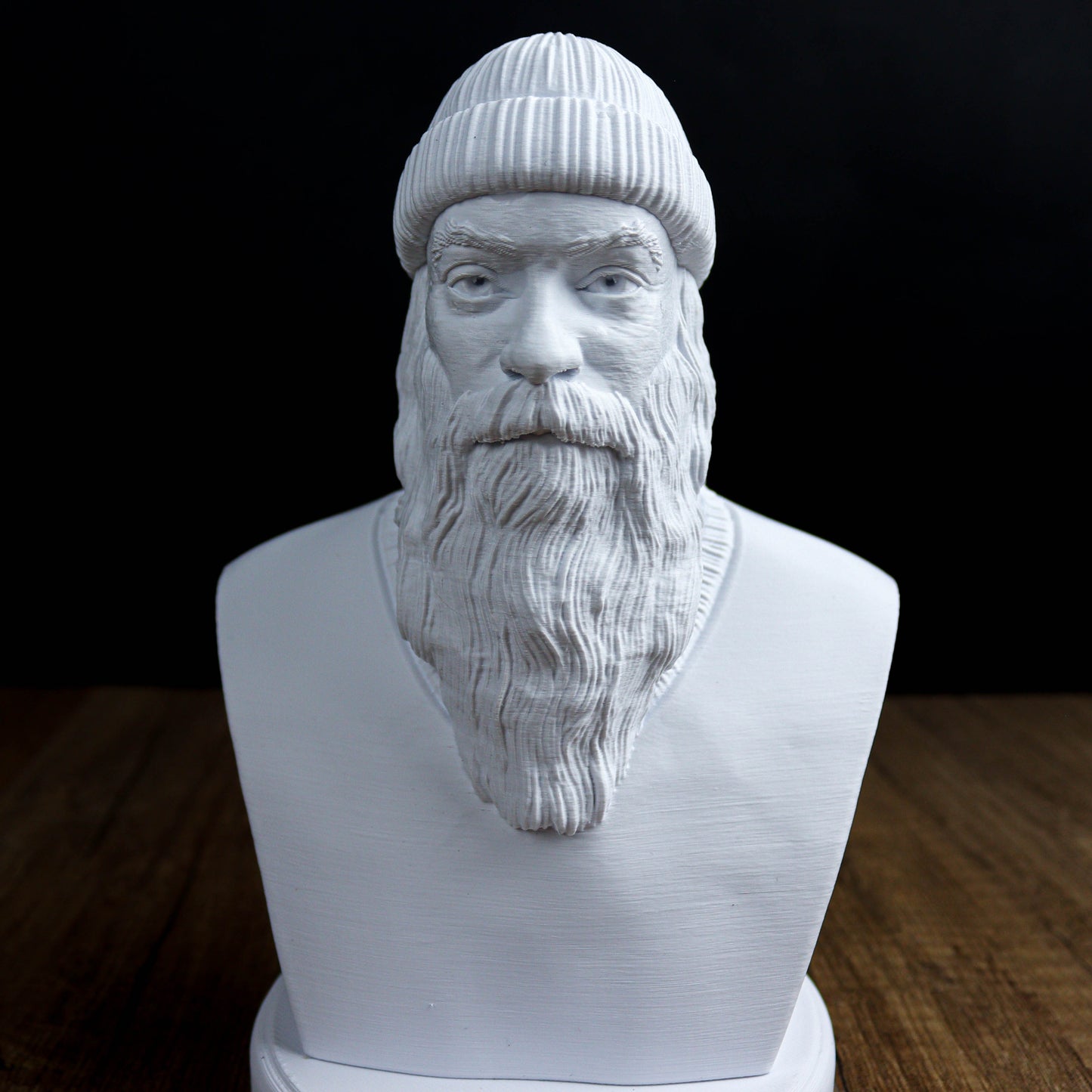 A white bust sculpture depicting a bearded man wearing a knit cap, set against a dark background.