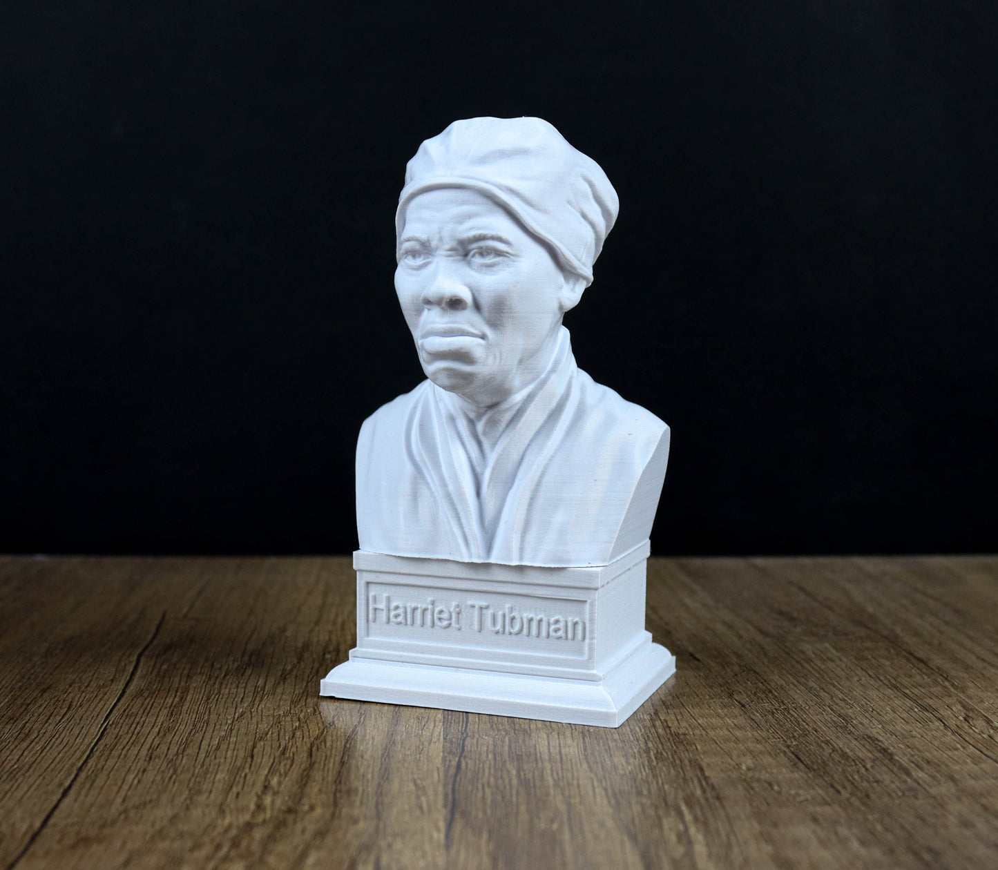 A white bust of a person, likely a historical figure, is displayed on a wooden surface against a black background.