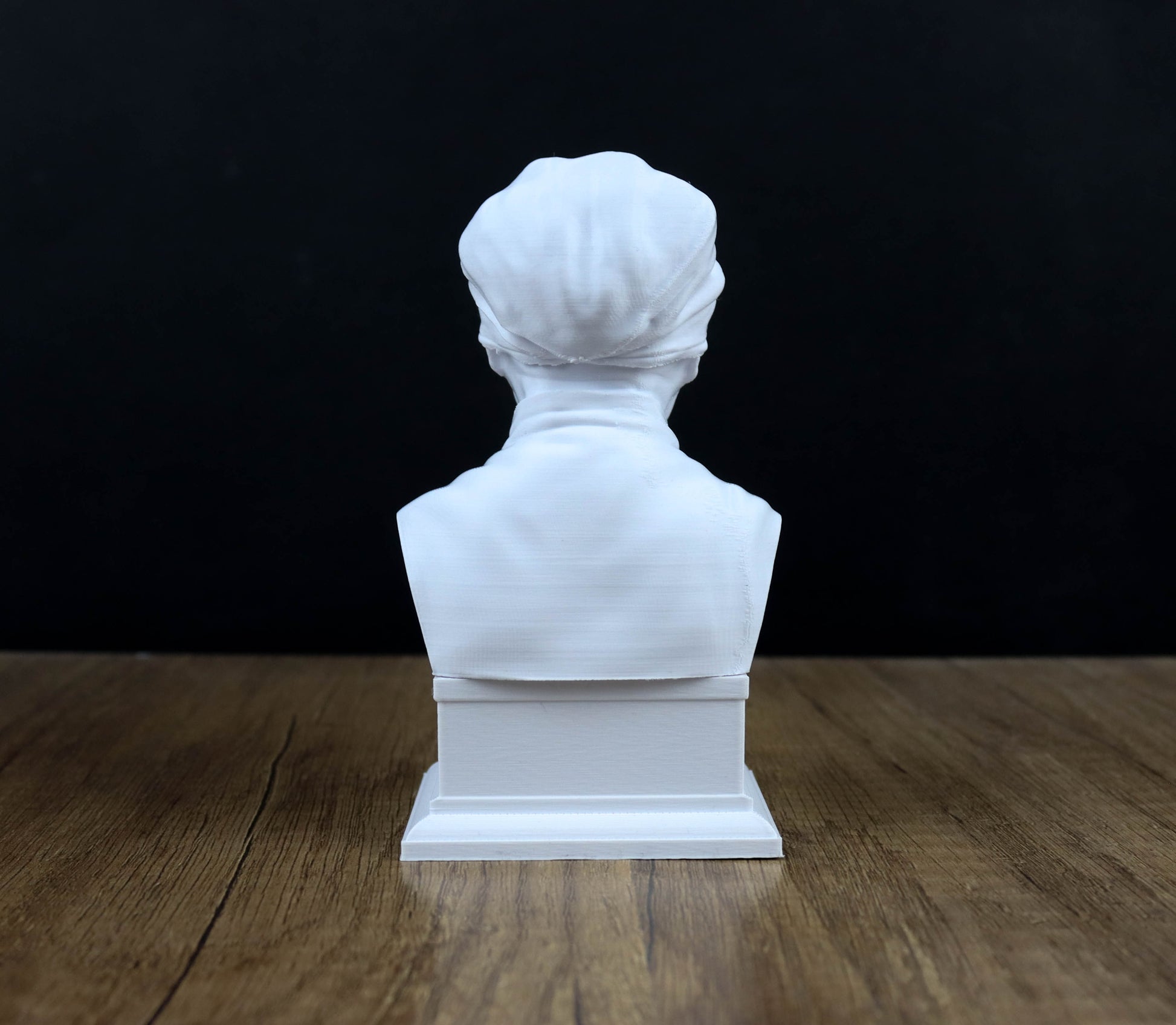 A white bust sculpture is displayed on a wooden surface against a black background.