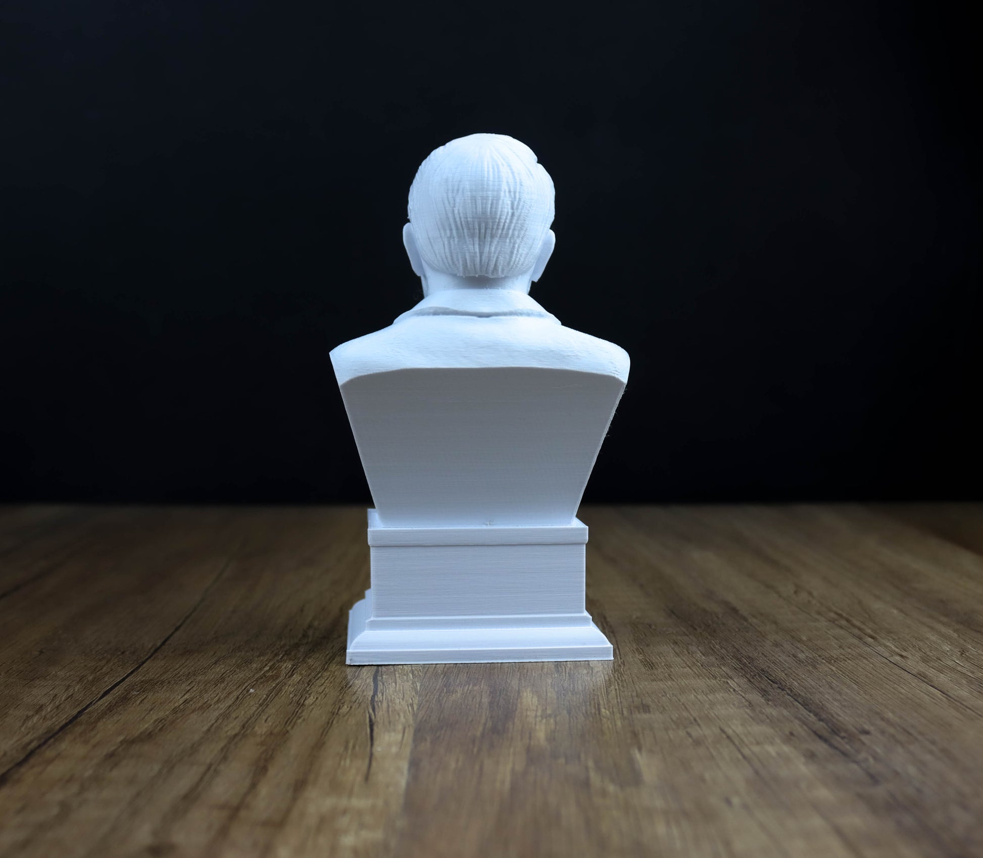 A white bust of a person sitting on a wooden surface against a dark background.