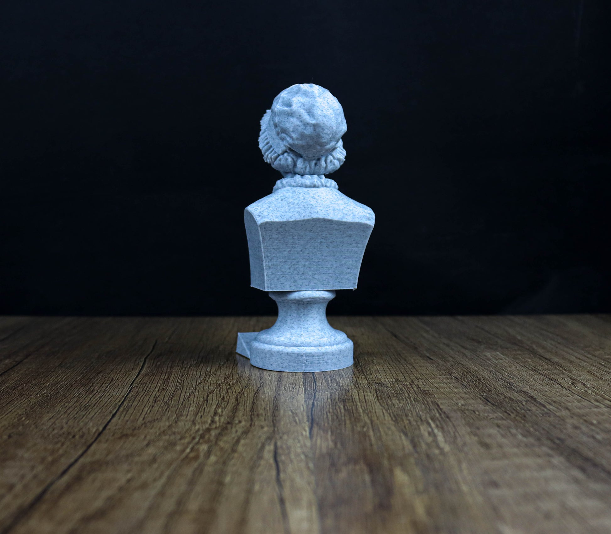 A white stone statue of a person is displayed on a wooden surface against a dark background.