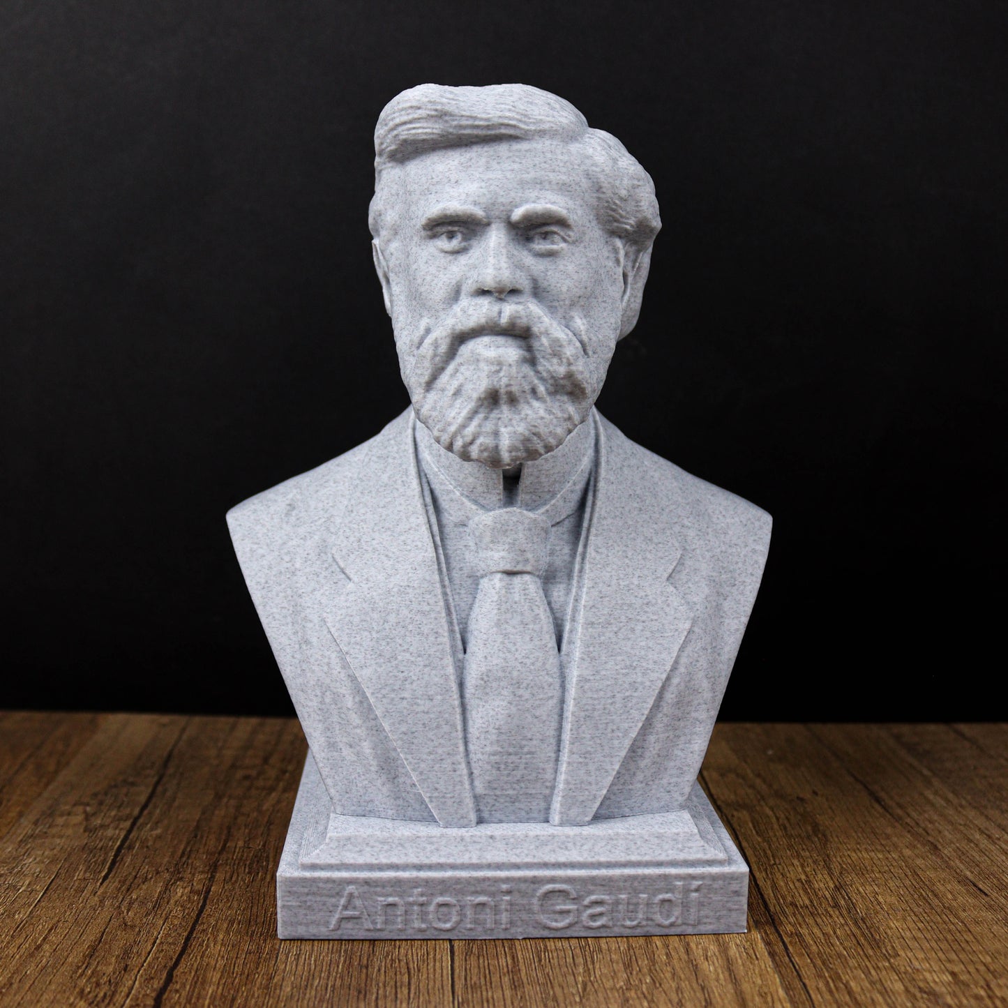 A bust of a bearded man wearing a suit and tie, with the name "Antoni Gaudi" engraved on the base.
