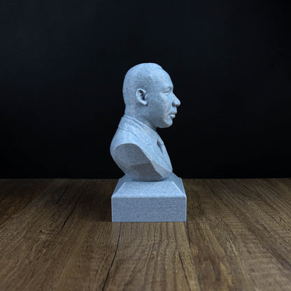 A gray bust of a person is sitting on a wooden surface against a black background.