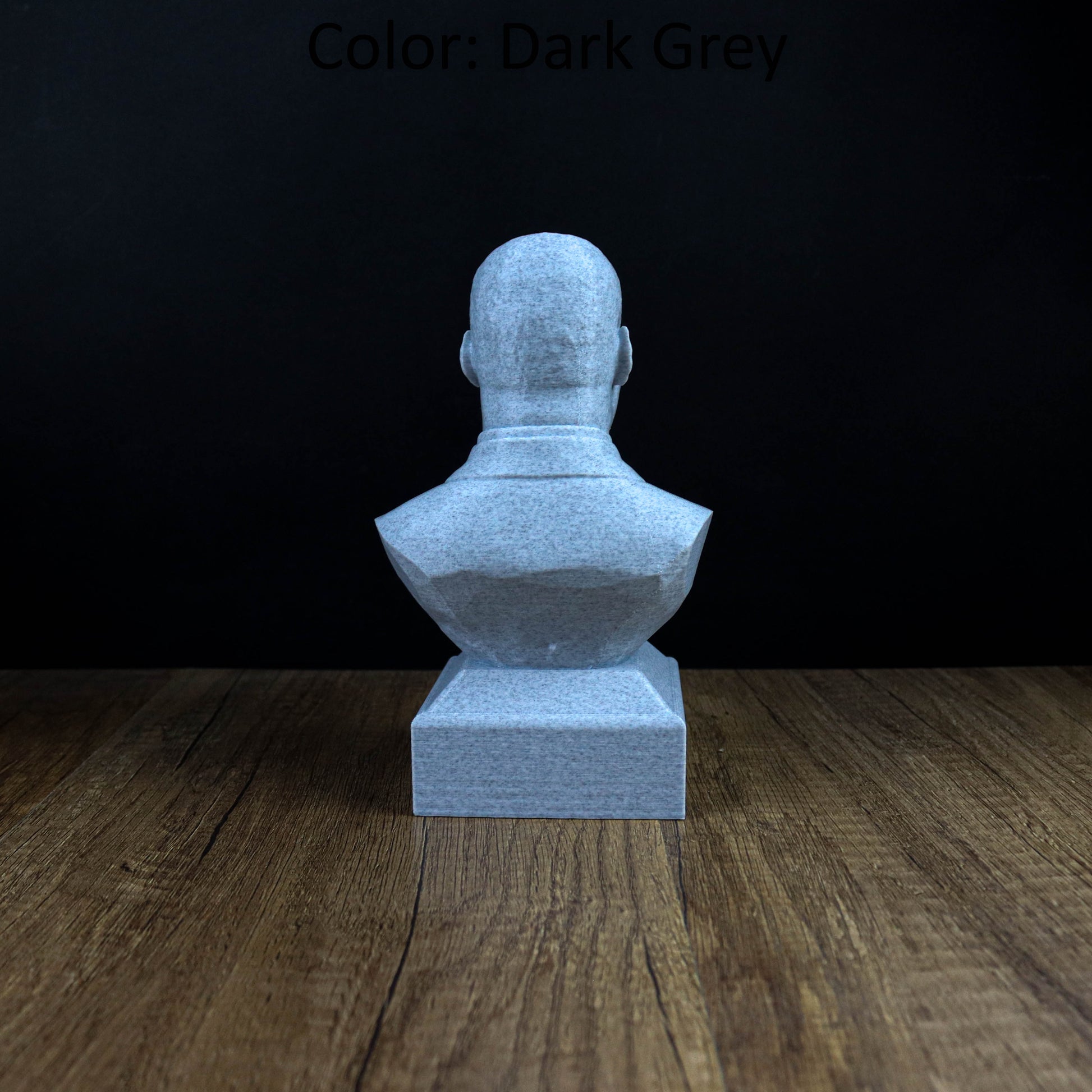 A gray stone bust sculpture is displayed on a wooden surface against a dark background.