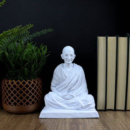 A white Buddha statue sits on a wooden surface, surrounded by a potted plant and a stack of books.