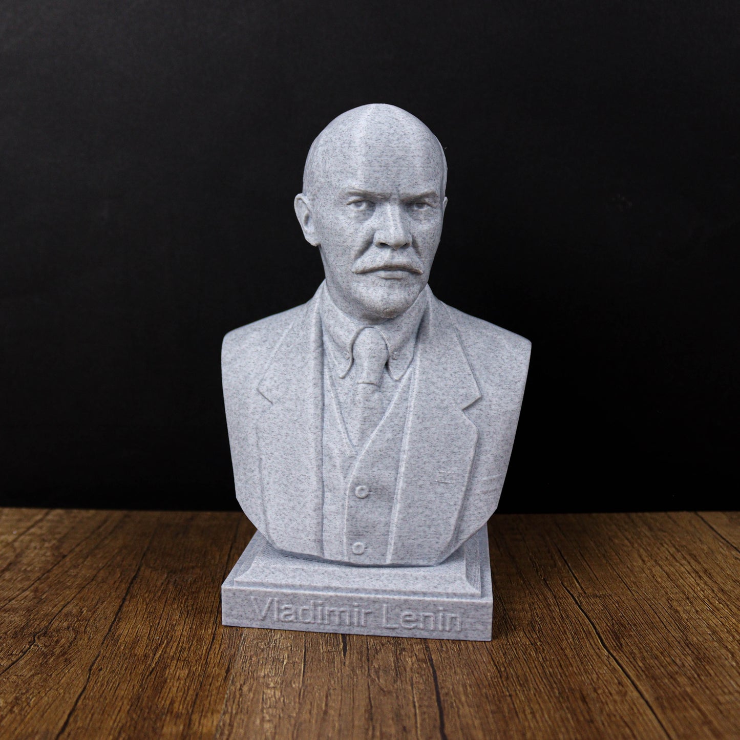 A bust of Vladimir Lenin, a prominent Russian political leader, is displayed on a wooden surface against a black background.