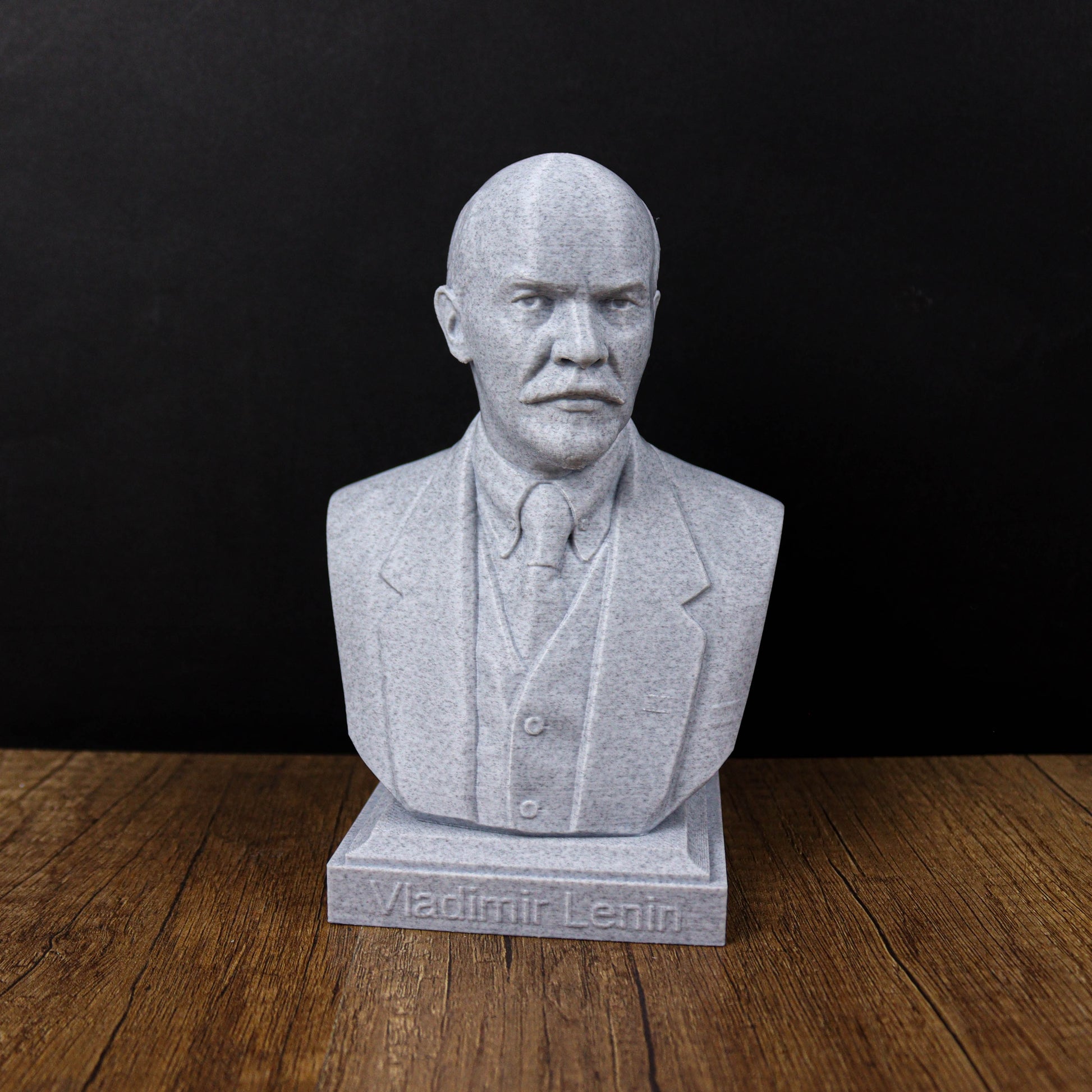 A bust of Vladimir Lenin, a prominent Russian political leader, is displayed on a wooden surface against a black background.