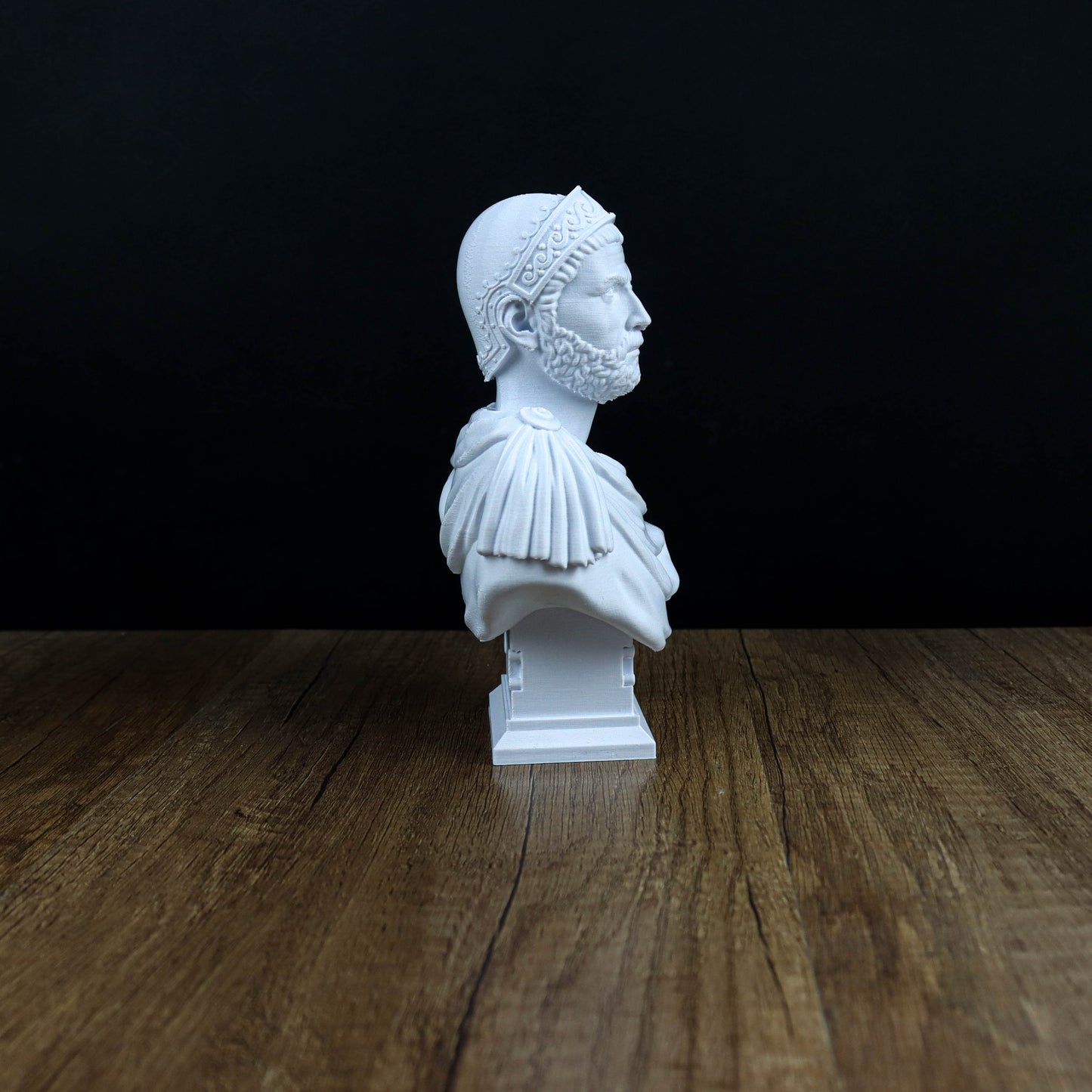 A white bust of a man with a beard and a headdress is displayed on a wooden surface against a black background.
