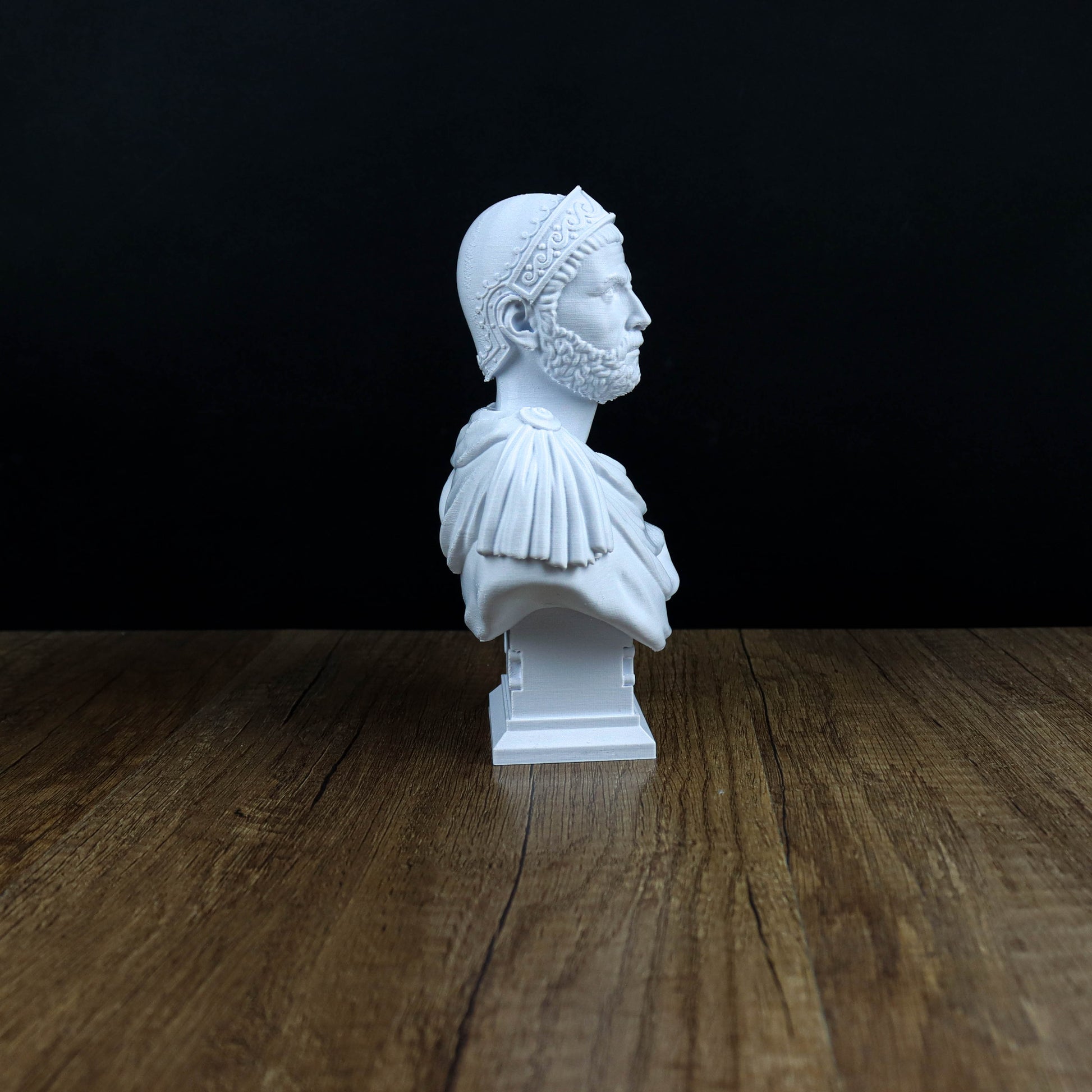 A white bust of a man with a beard and a headdress is displayed on a wooden surface against a black background.