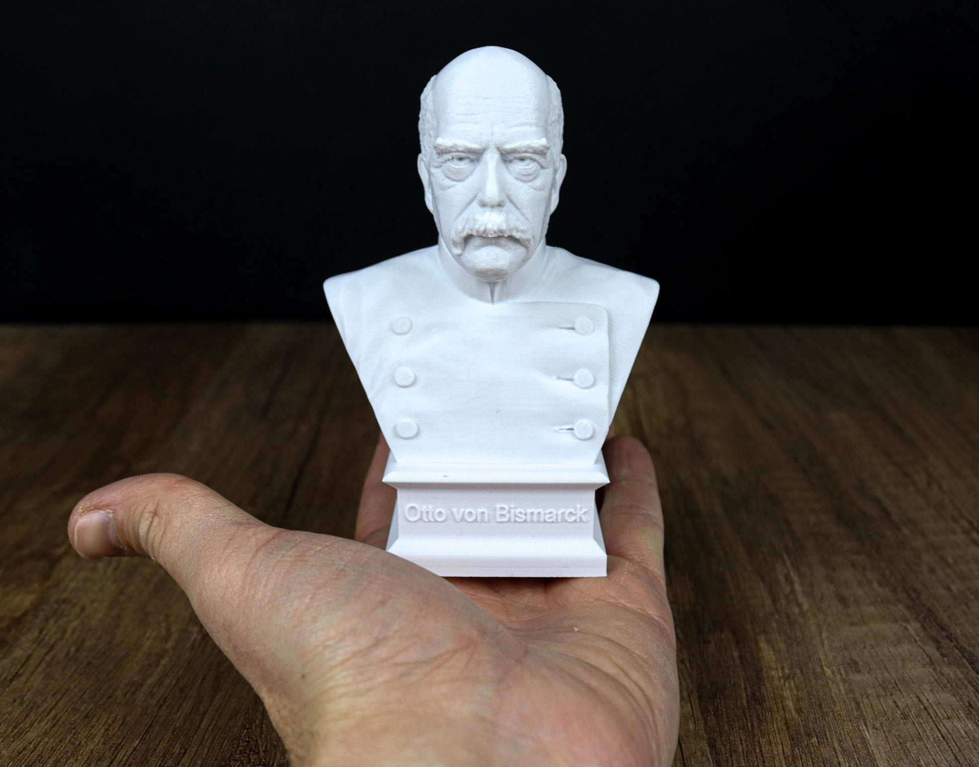 A white bust of a man is being held in a hand against a dark background.