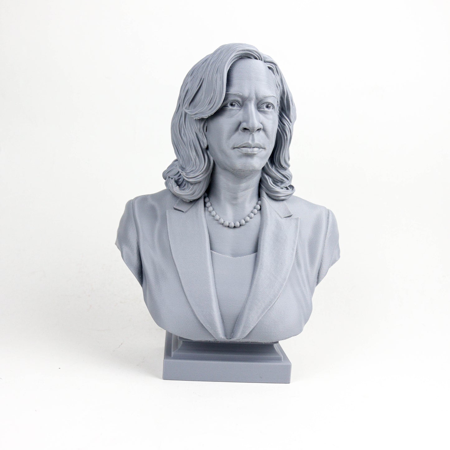 A gray bust sculpture of a woman with long hair and a pearl necklace, wearing a jacket.