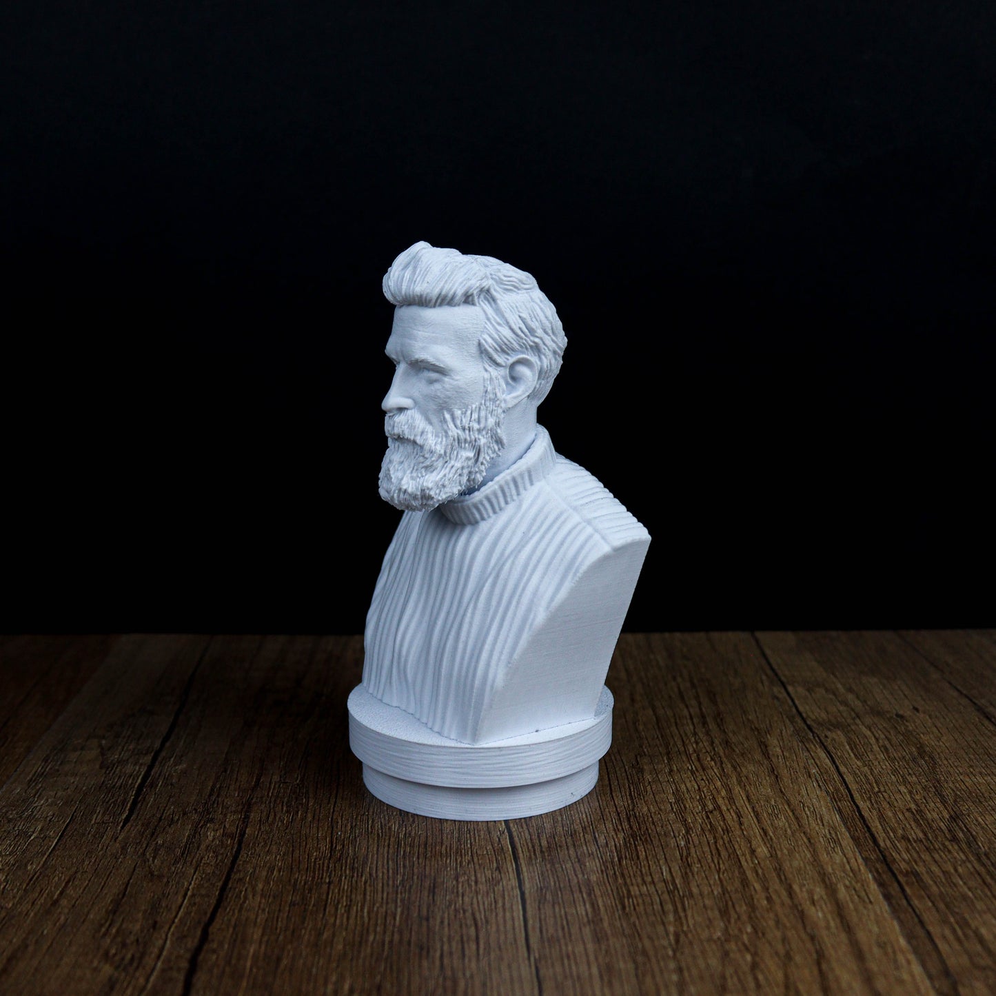 A white bust of a bearded man is displayed on a wooden surface against a dark background.