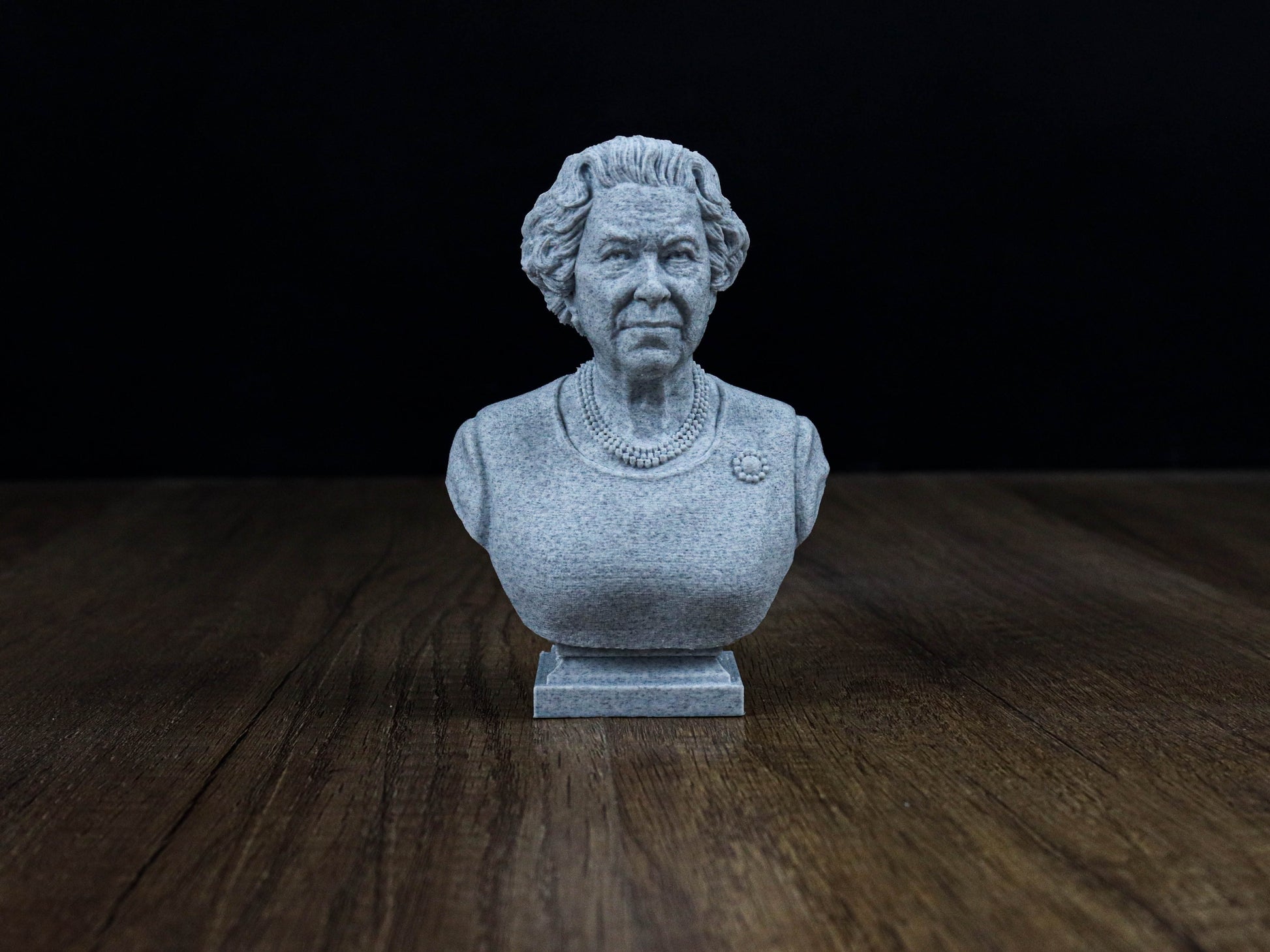 A small gray stone bust of a woman is displayed on a wooden surface against a dark background.