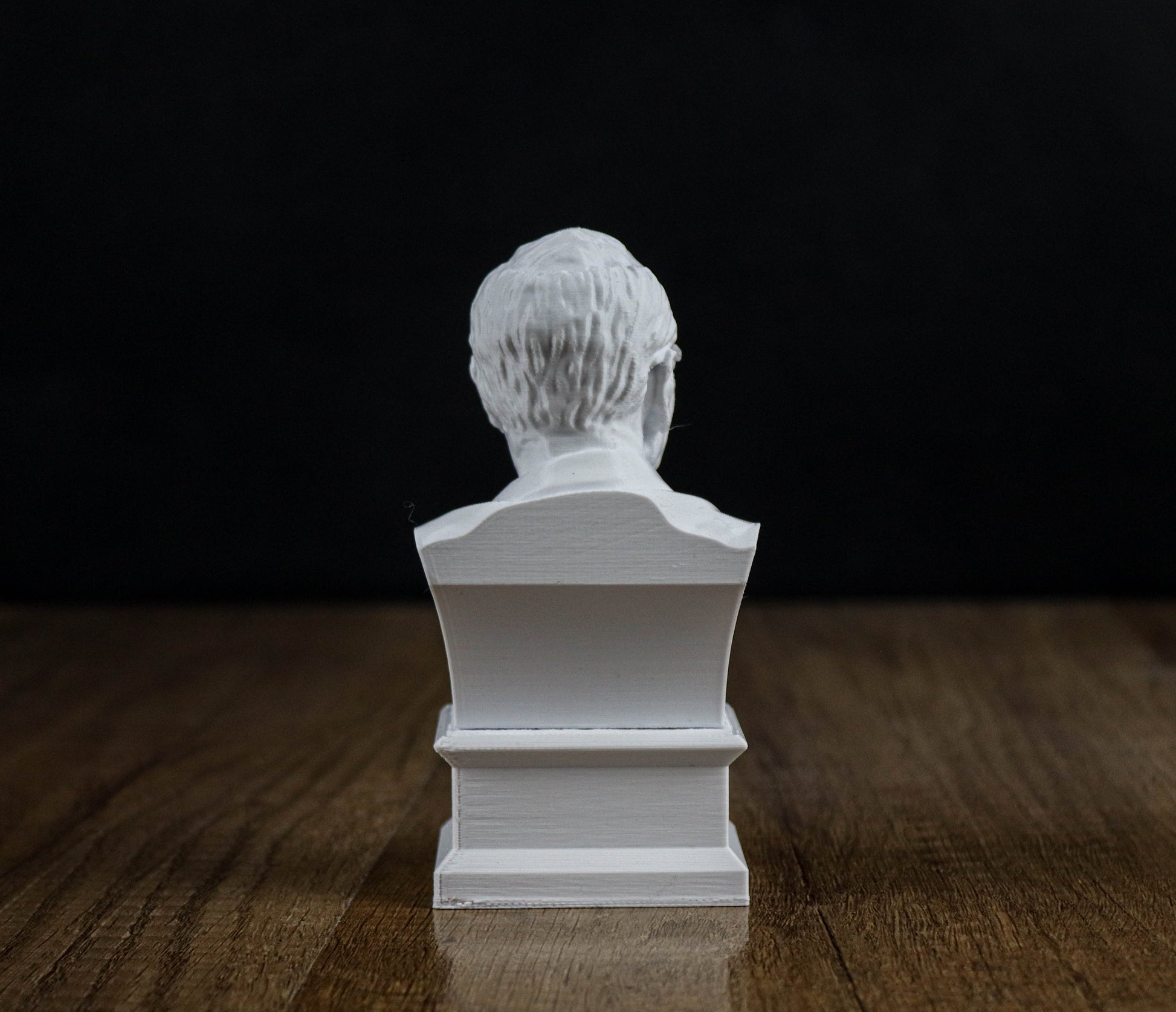 A white bust of a person sitting on a wooden surface against a black background.