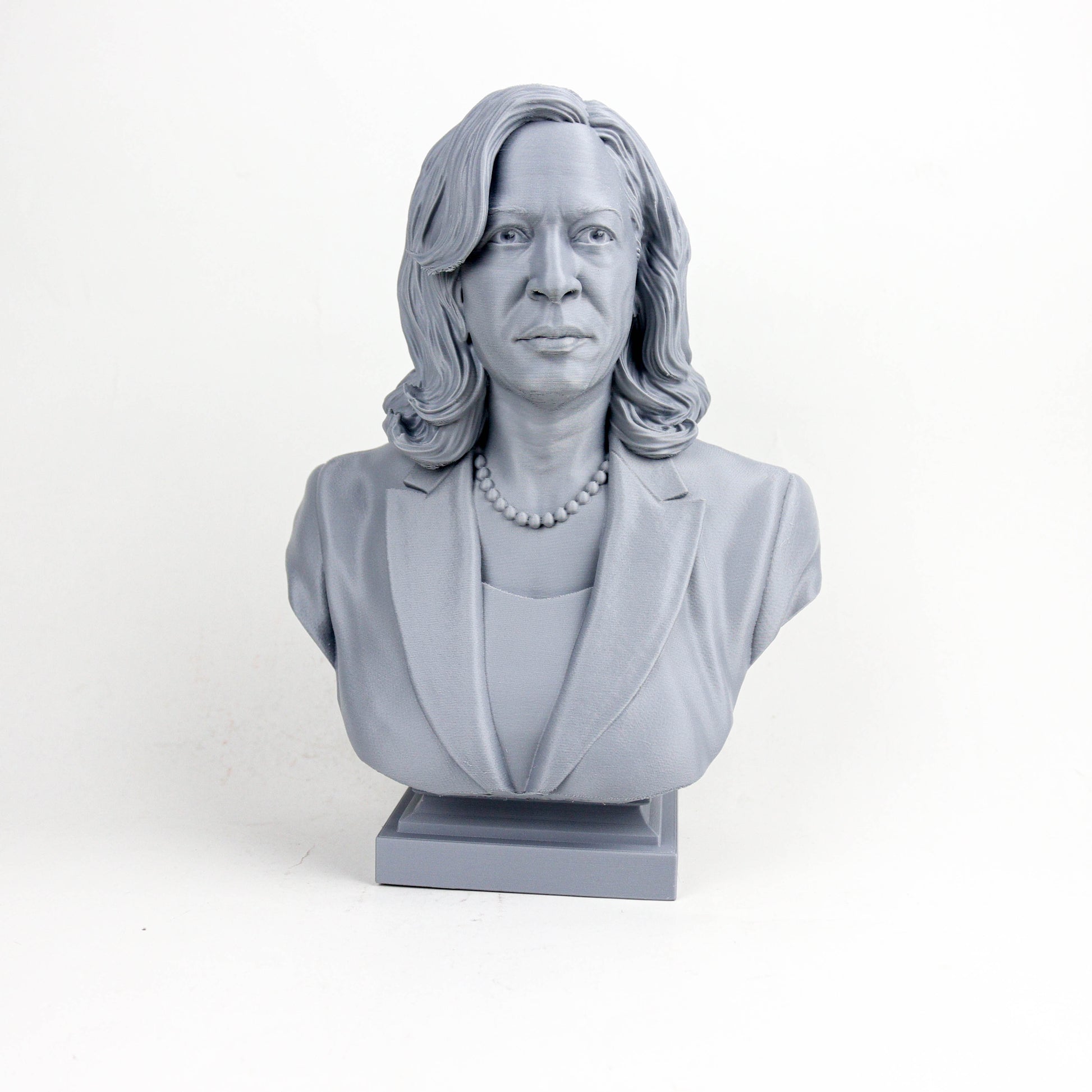 A gray bust sculpture of a woman with long hair and a pearl necklace, wearing a jacket.