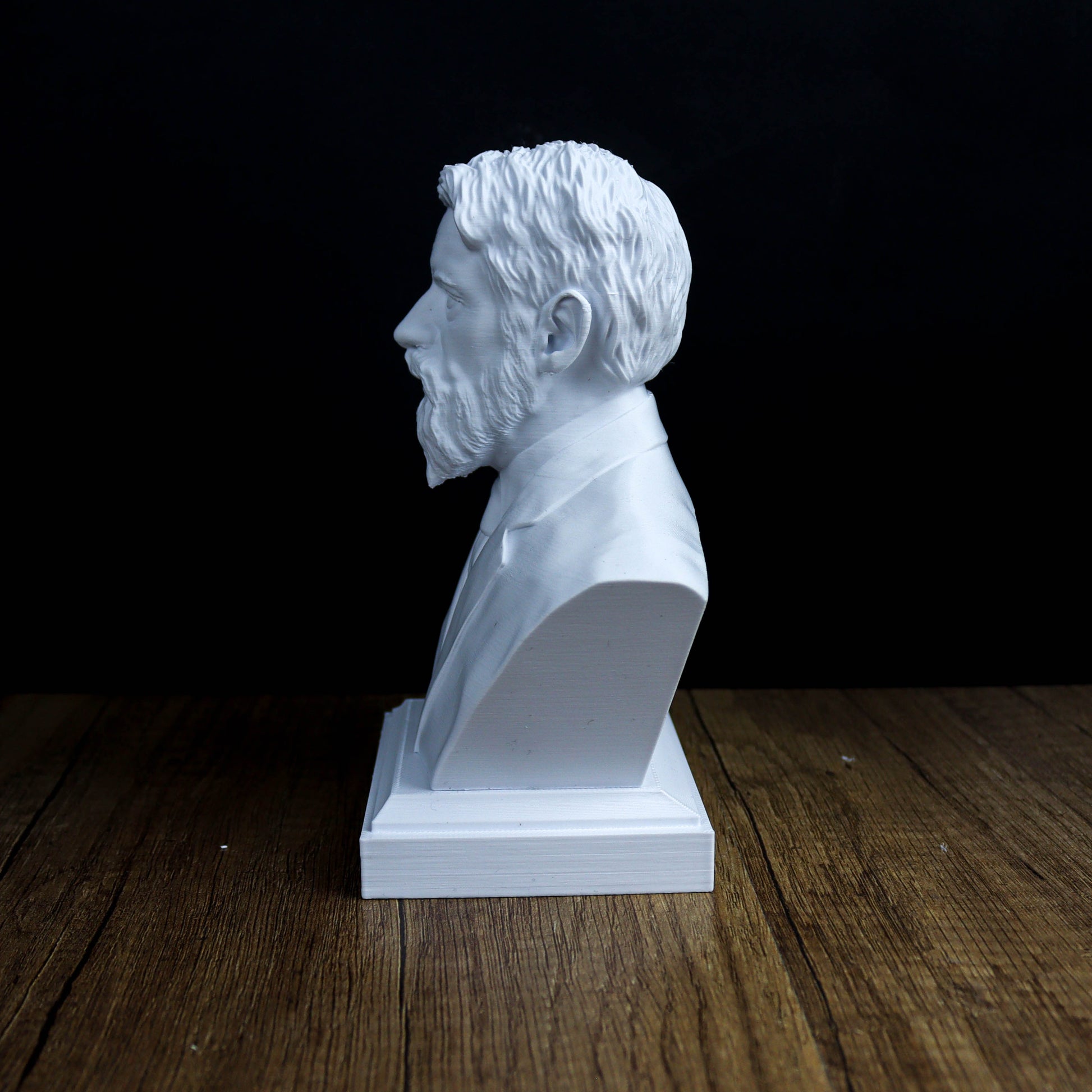 A white bust of a man's head is displayed on a wooden surface against a dark background.