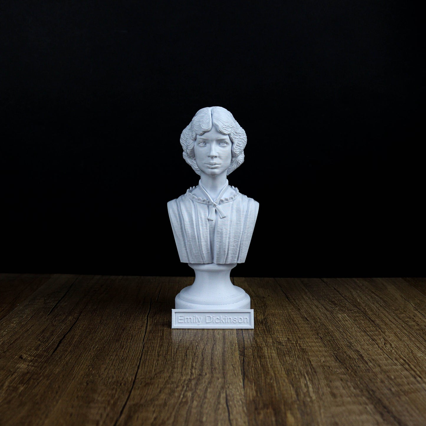 A white bust of a person, likely a historical figure, is displayed on a wooden surface against a black background.