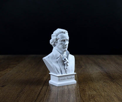 A white bust of a man, likely Alexander Hamilton, is displayed on a wooden surface against a dark background.