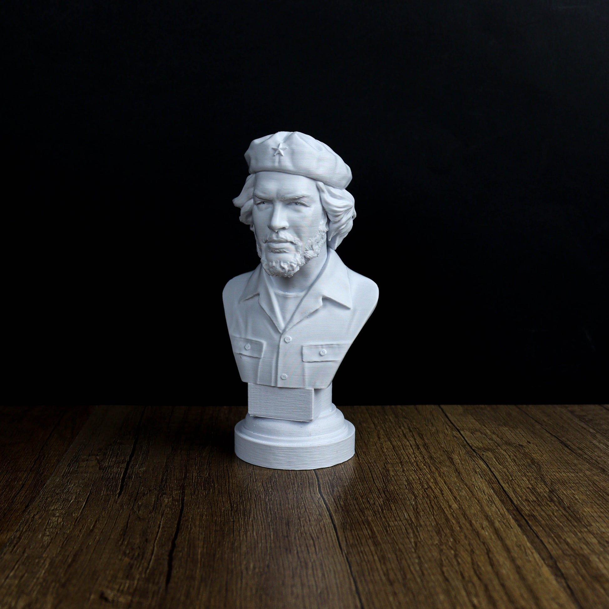 A white bust of a man with a beard and hat, possibly representing a historical figure, is displayed on a wooden surface against a black background.
