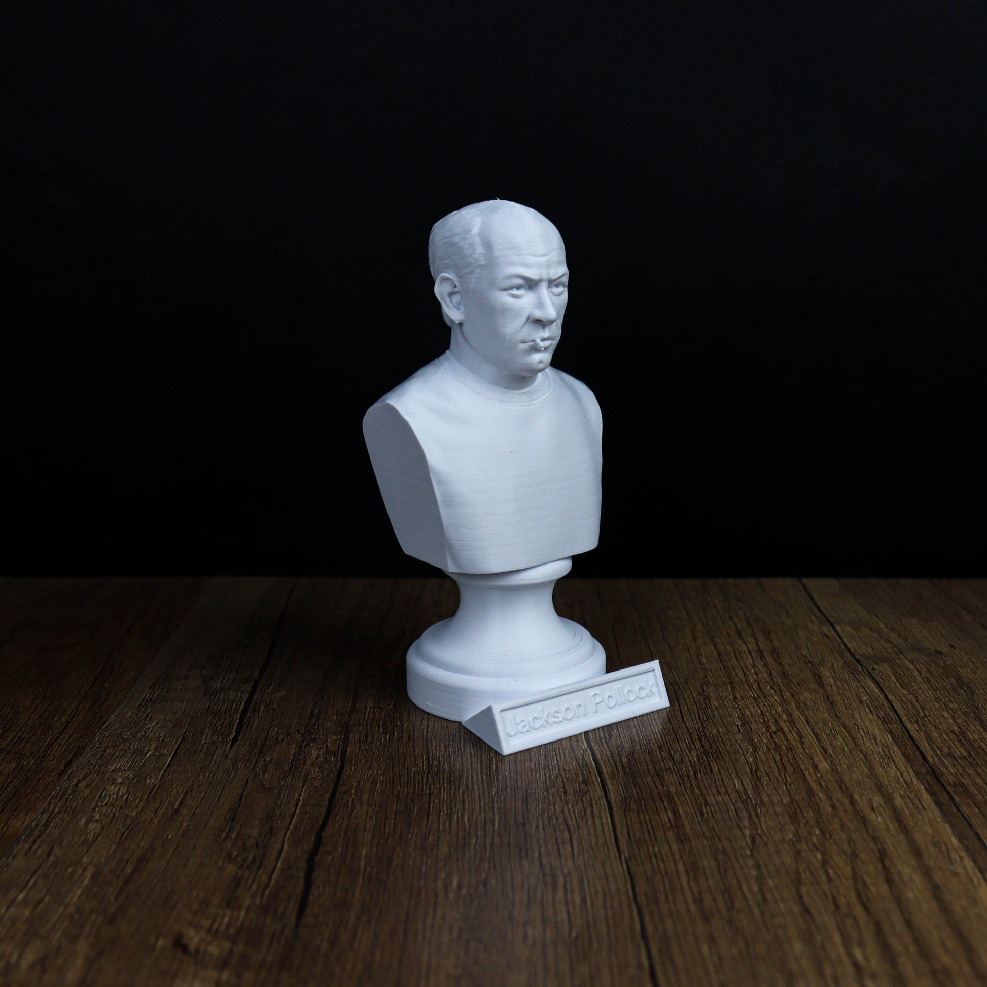 A white bust of a person is sitting on a wooden surface against a black background.