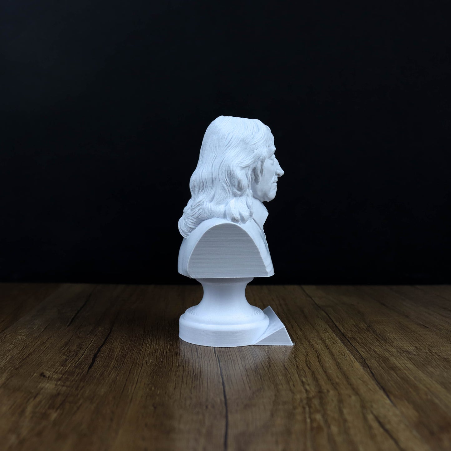 A white bust of a person is displayed on a wooden surface against a dark background.