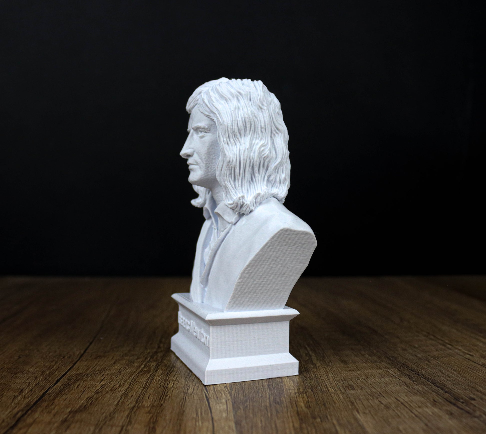 A white bust of a person with long hair is displayed on a wooden surface against a black background.