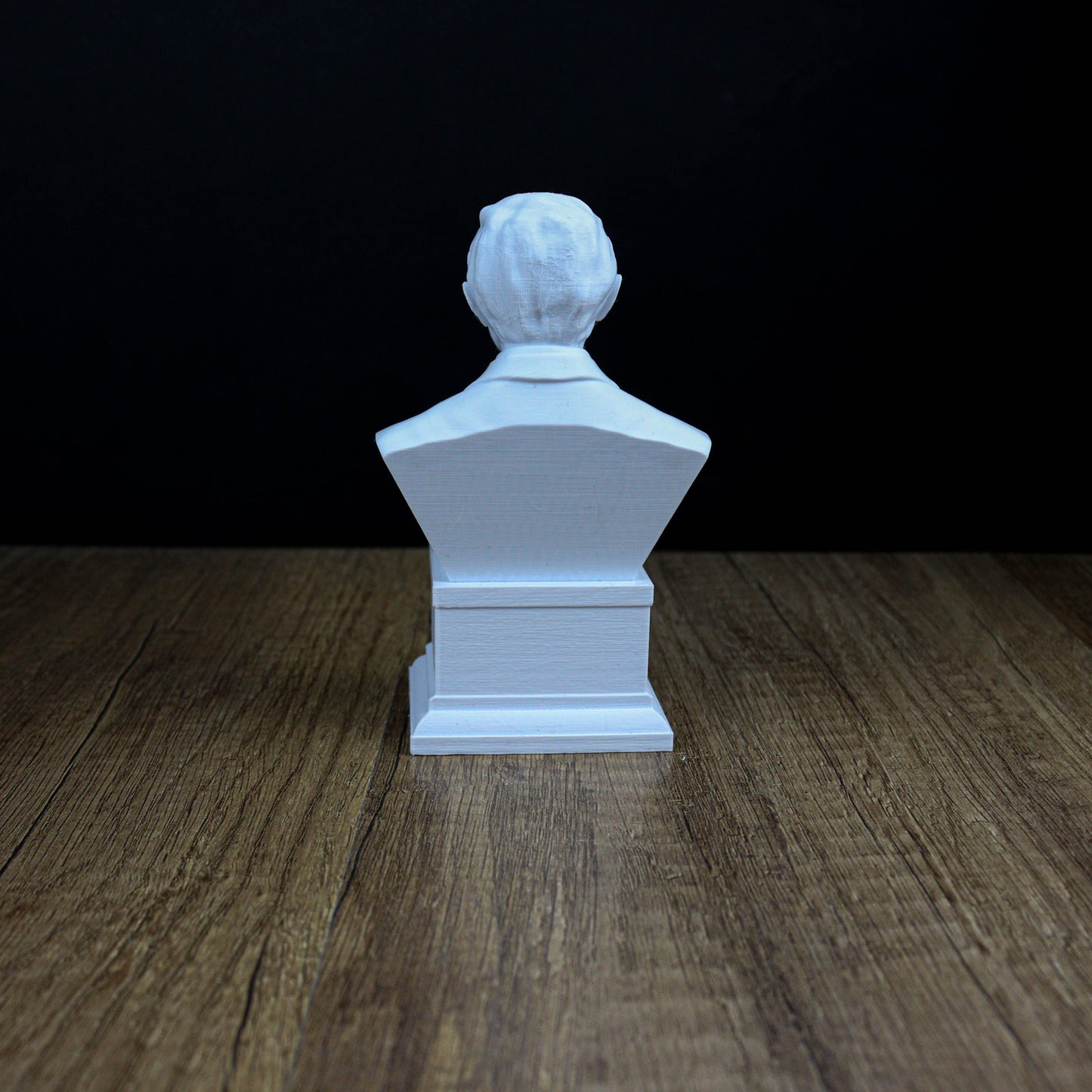 A white bust of a person sitting on a wooden surface against a dark background.