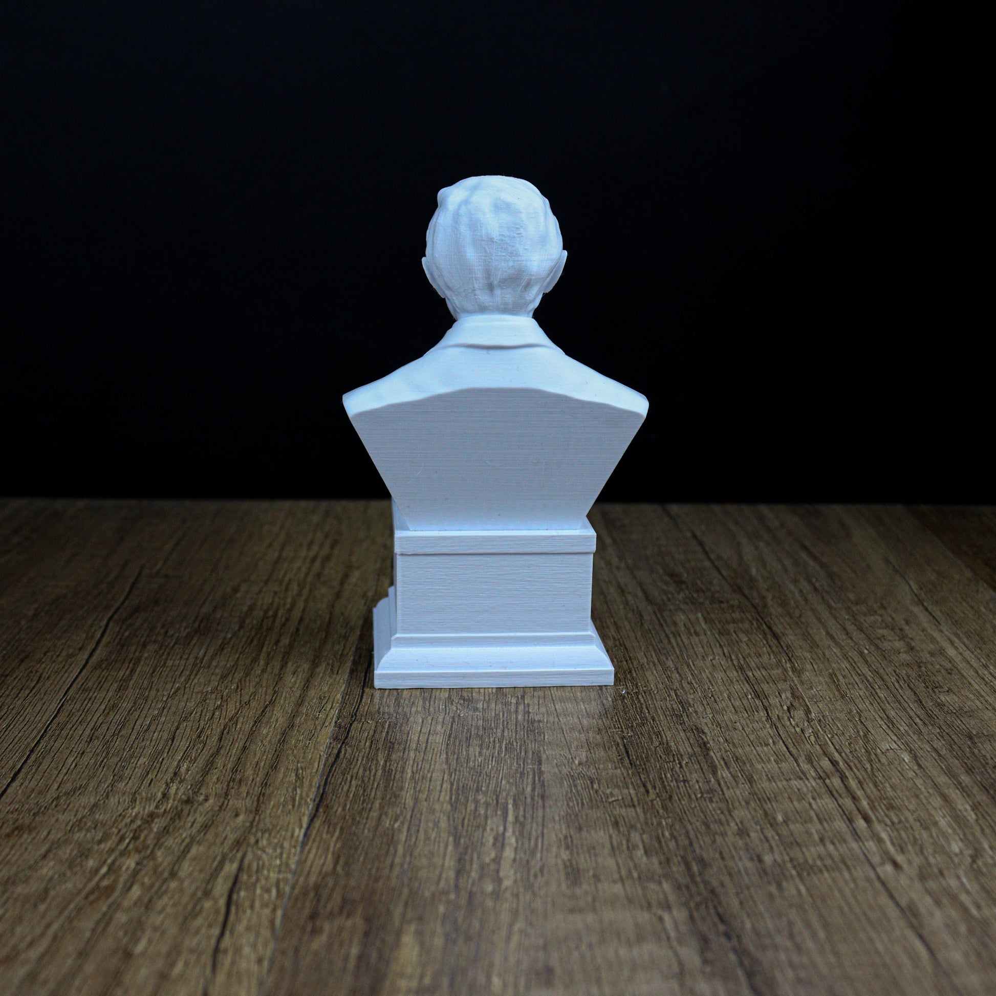 A white bust of a person sitting on a wooden surface against a dark background.