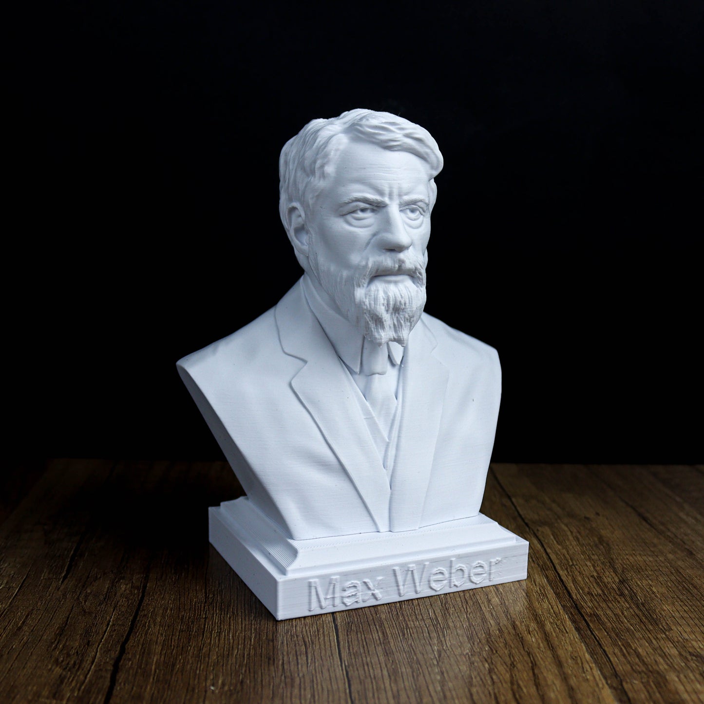 A white bust of a bearded man wearing a suit, sitting on a wooden surface.