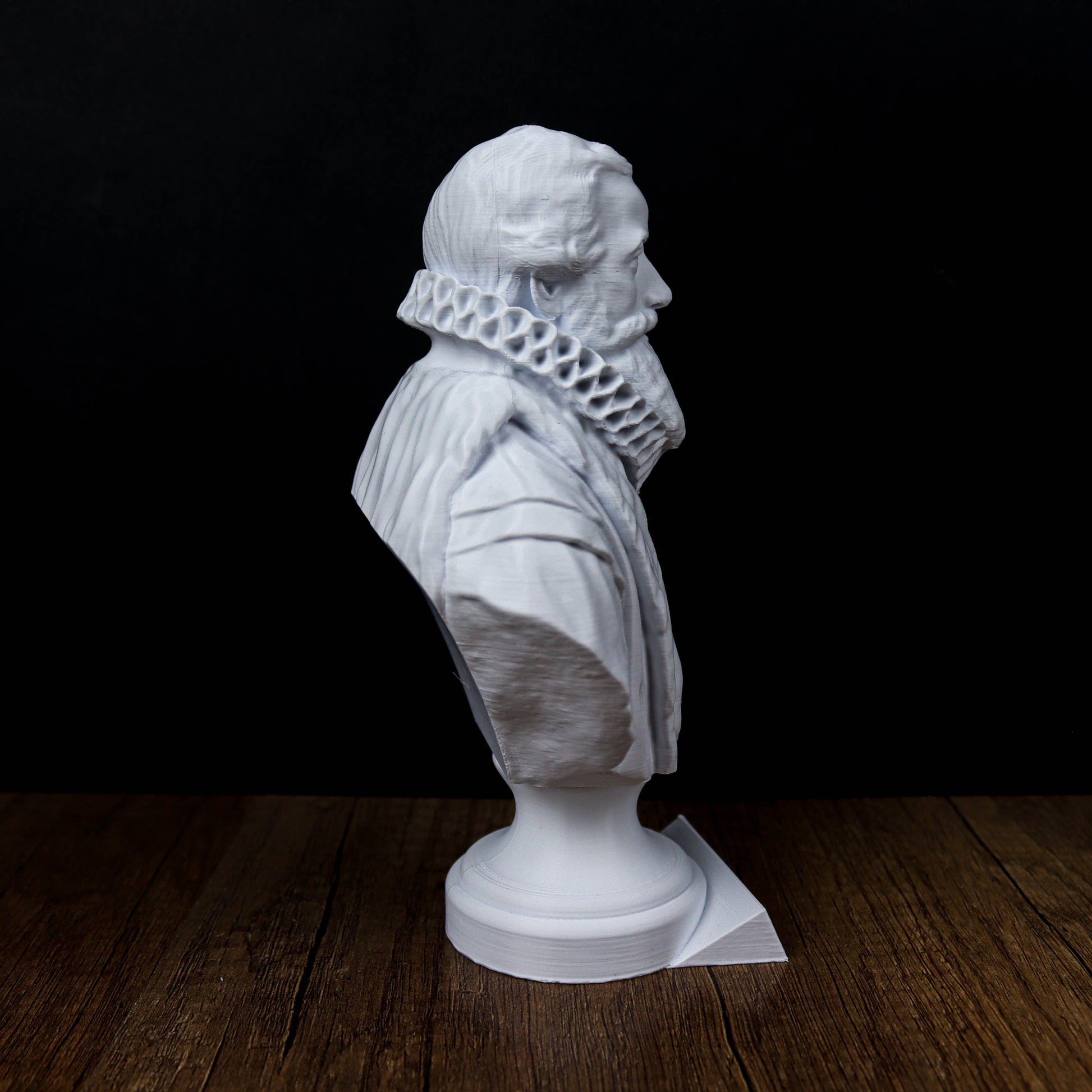 A white bust of a man with a beard is displayed on a wooden surface against a black background.