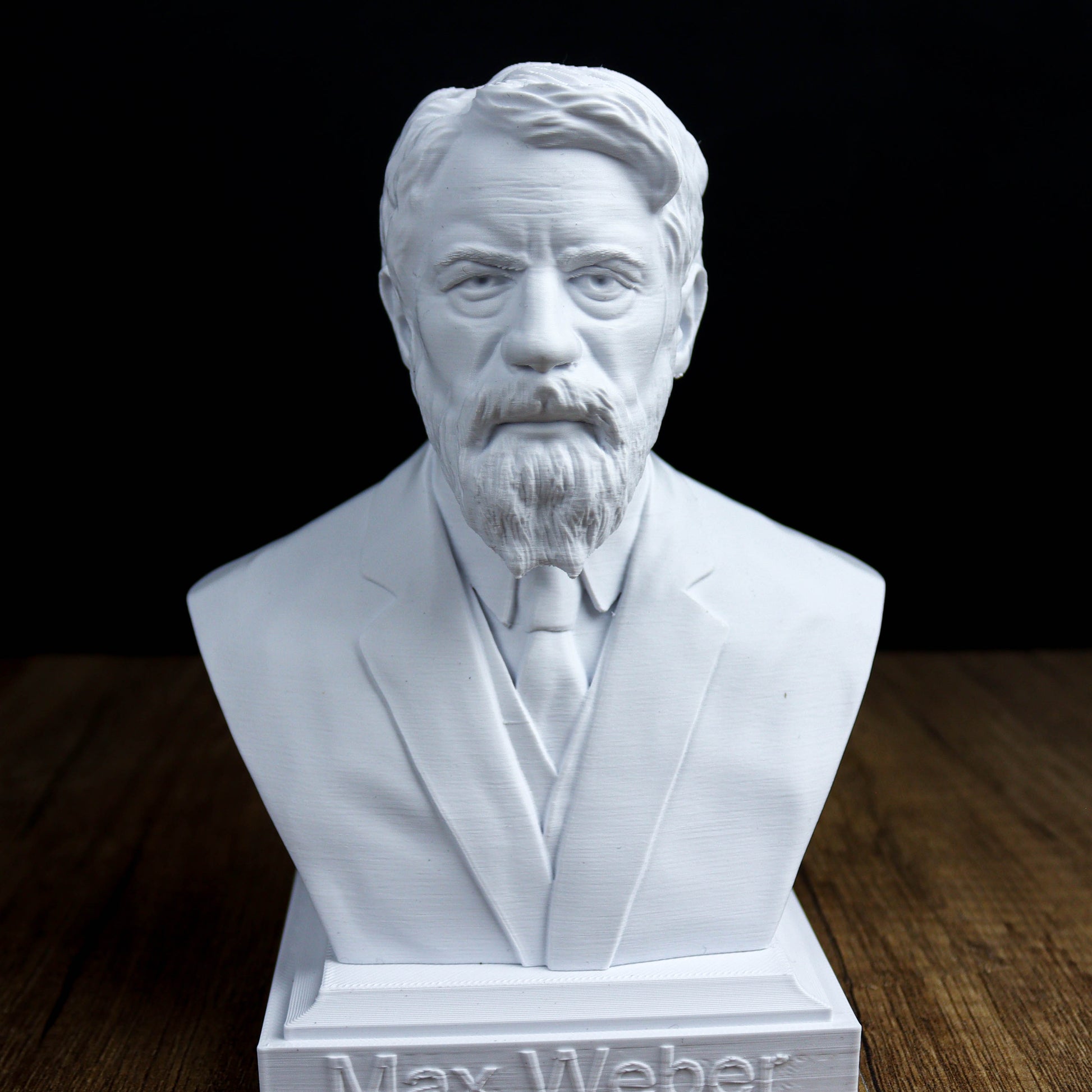 A white bust sculpture of a man with a beard and mustache, wearing a suit and tie, sitting on a wooden surface.