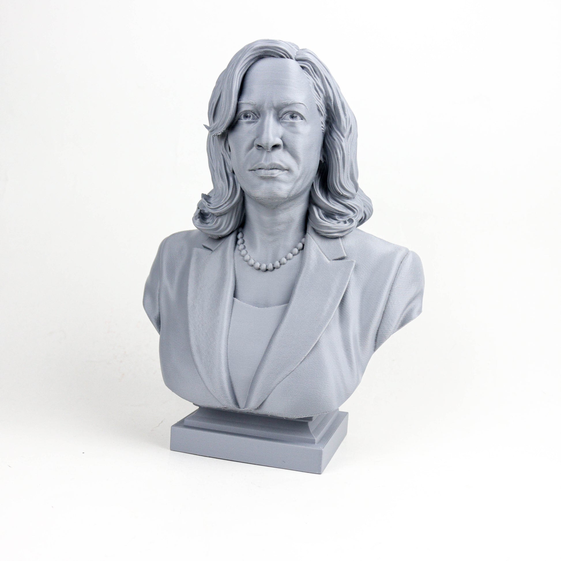 A gray bust sculpture of a woman with long hair and a pearl necklace, wearing a jacket.