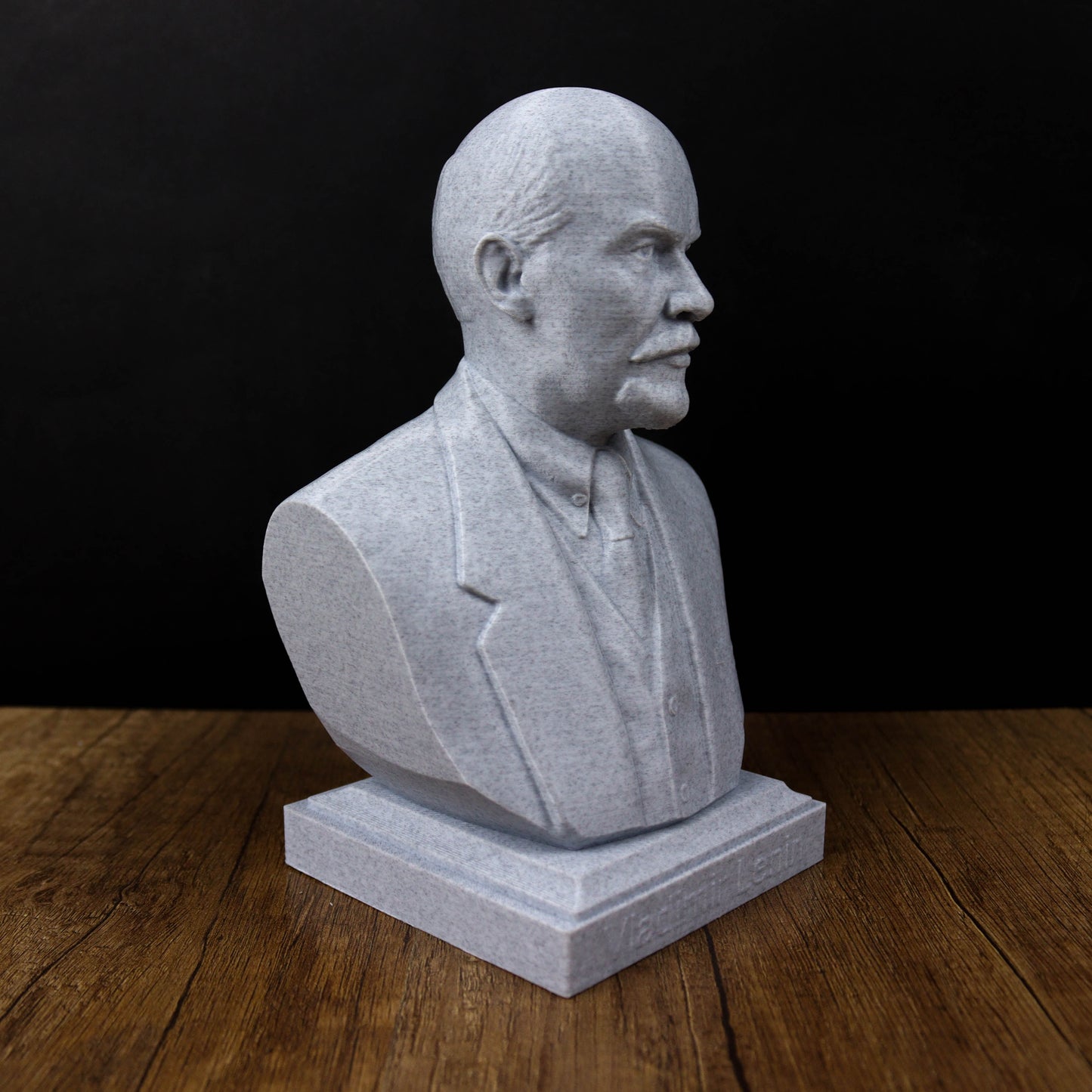 A gray stone bust of a man wearing a suit and tie, sitting on a wooden surface.