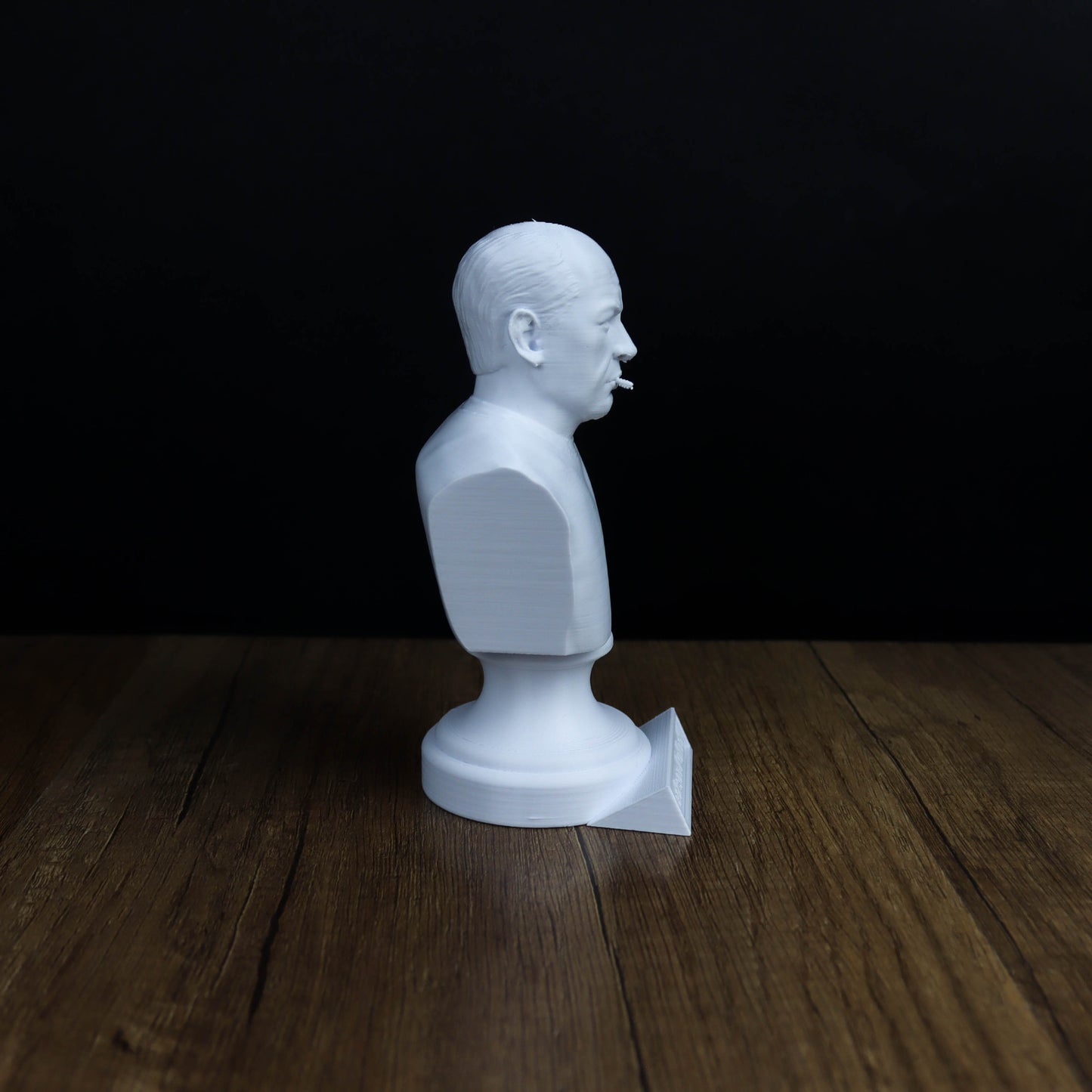 A white bust figurine is sitting on a wooden surface against a dark background.
