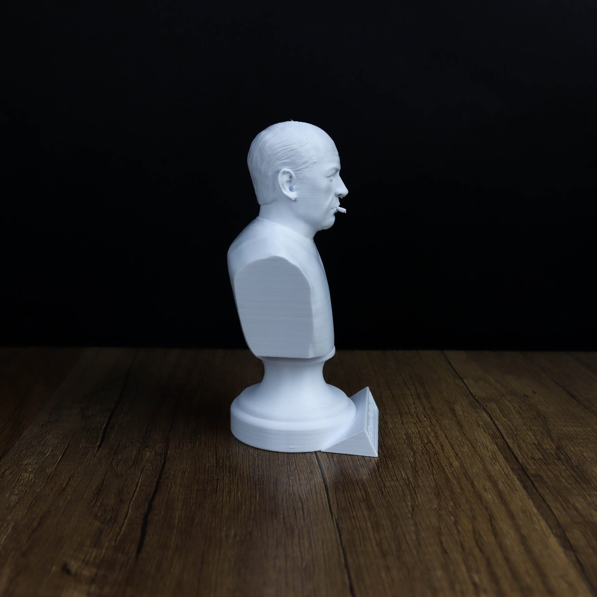 A white bust figurine is sitting on a wooden surface against a dark background.