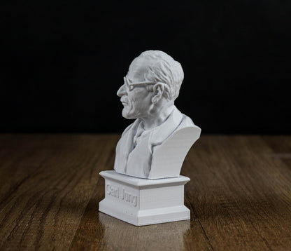 A white bust of a man wearing glasses is displayed on a wooden surface against a black background.