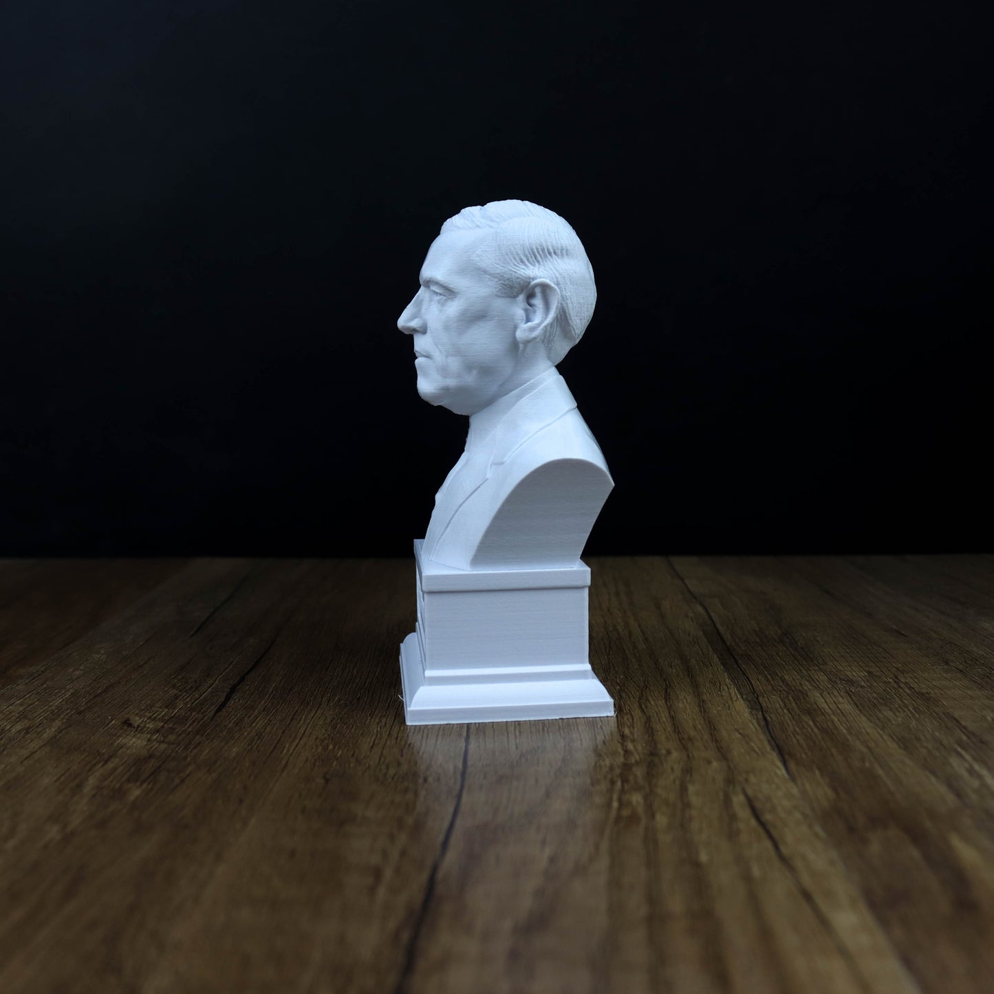 A white bust of a man is displayed on a wooden surface against a dark background.