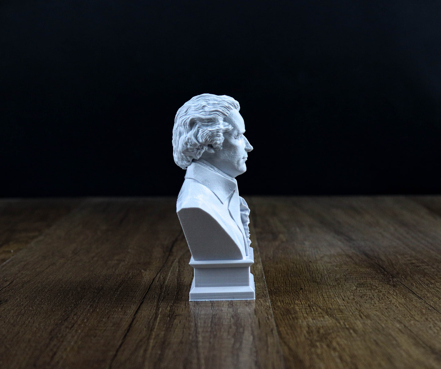 A white bust of a man is displayed on a wooden surface against a dark background.