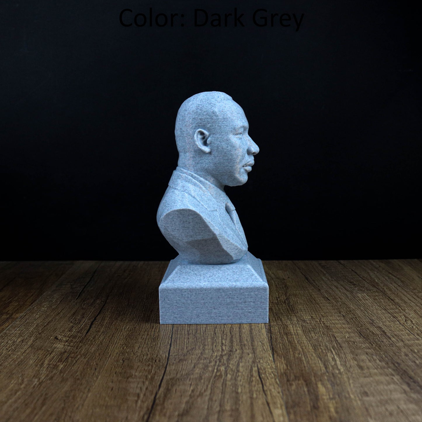 A gray stone bust statue of a man is displayed on a wooden surface against a dark background.